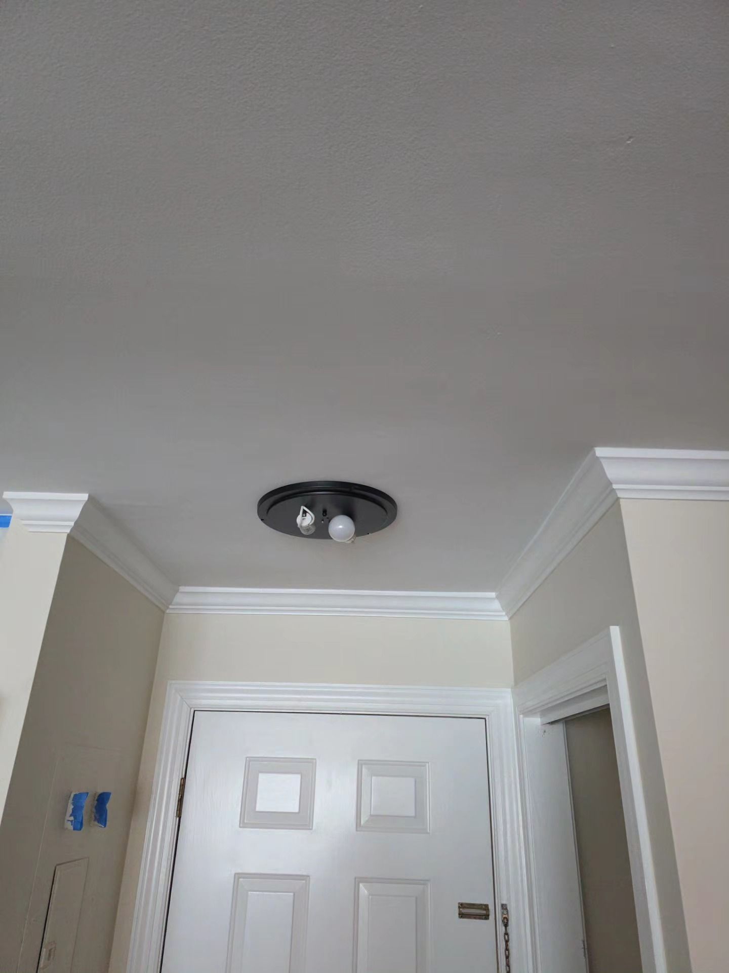 Interior hallway with white double doors, beige walls, crown molding, and a ceiling light fixture.