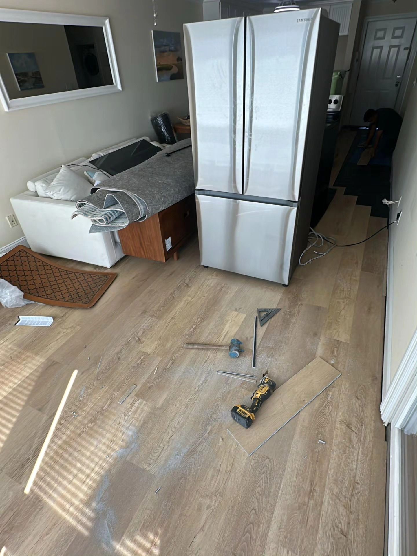 Messy kitchen with a stainless steel refrigerator, open trash bin, and tools on a wood floor during repairs