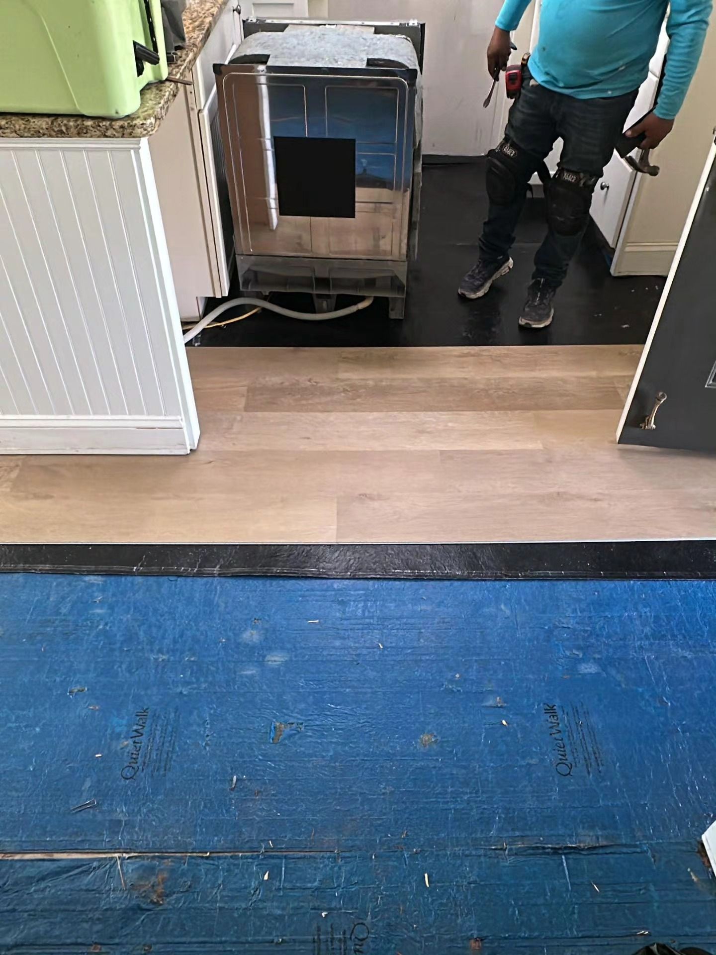 Two workers moving a large cart through a doorway onto a wood floor, with blue carpet in the foreground