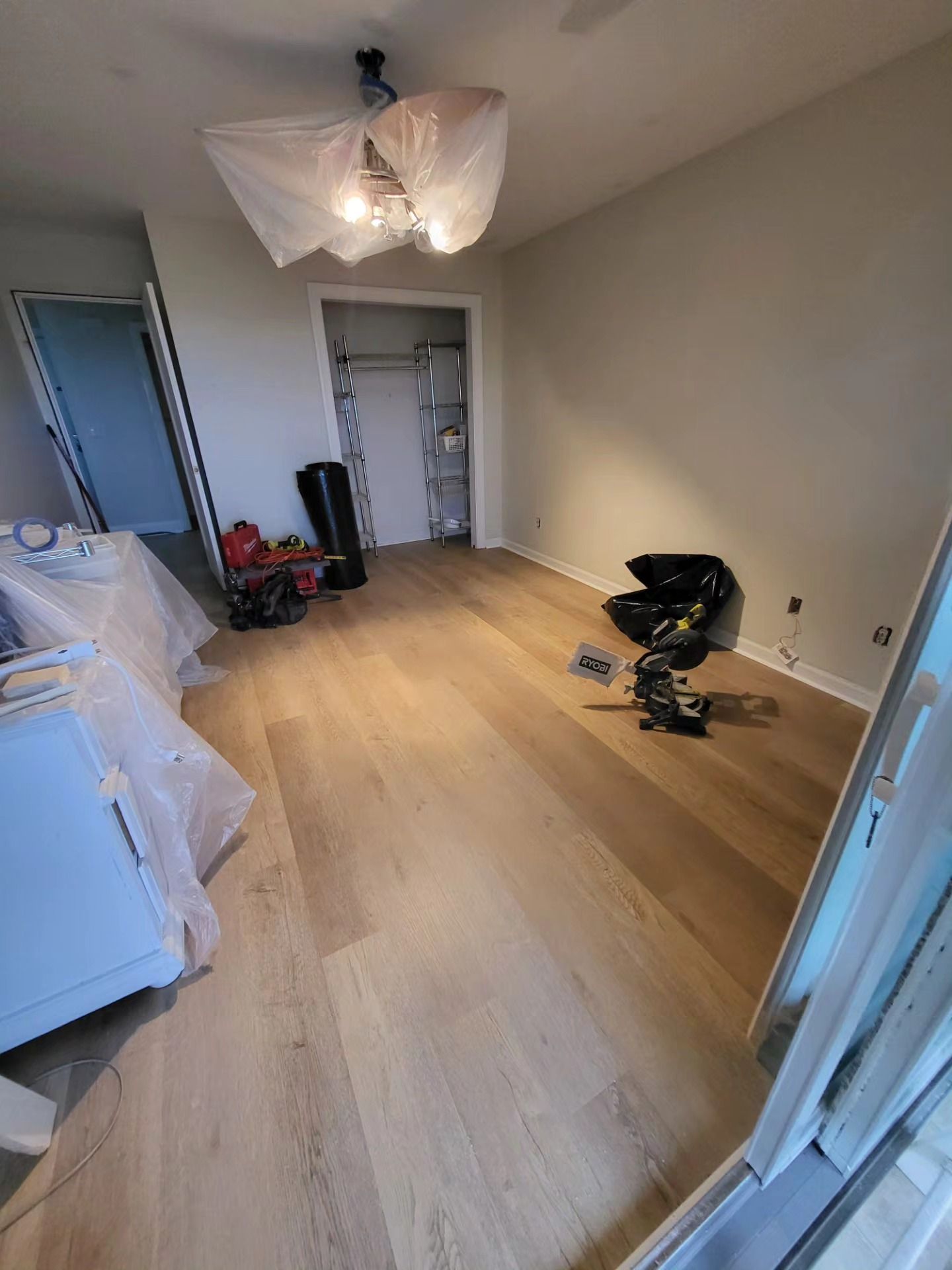 Empty room with light wood floors, white walls, a ceiling fan, and a few items scattered near the closet.