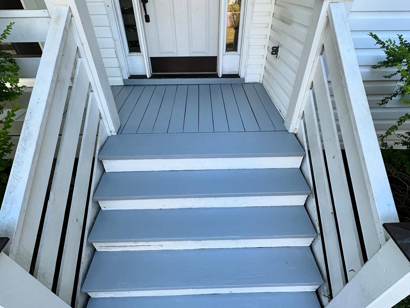 Gray front porch stairs leading to a white house entrance with a wooden deck and door