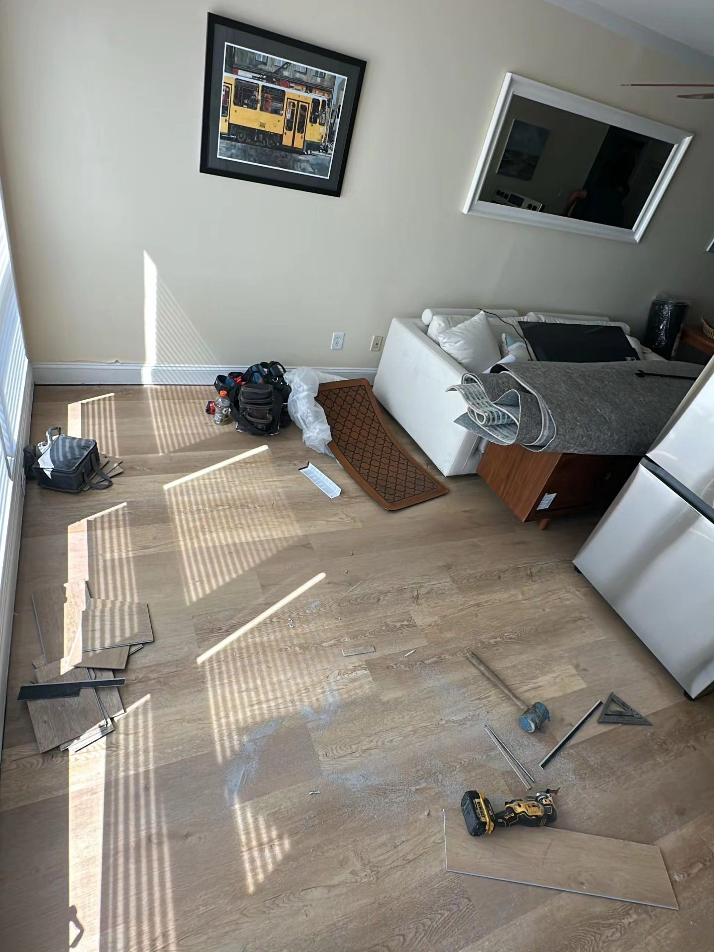 Messy living room with scattered tools, broken blinds, and a disassembled couch near a fridge