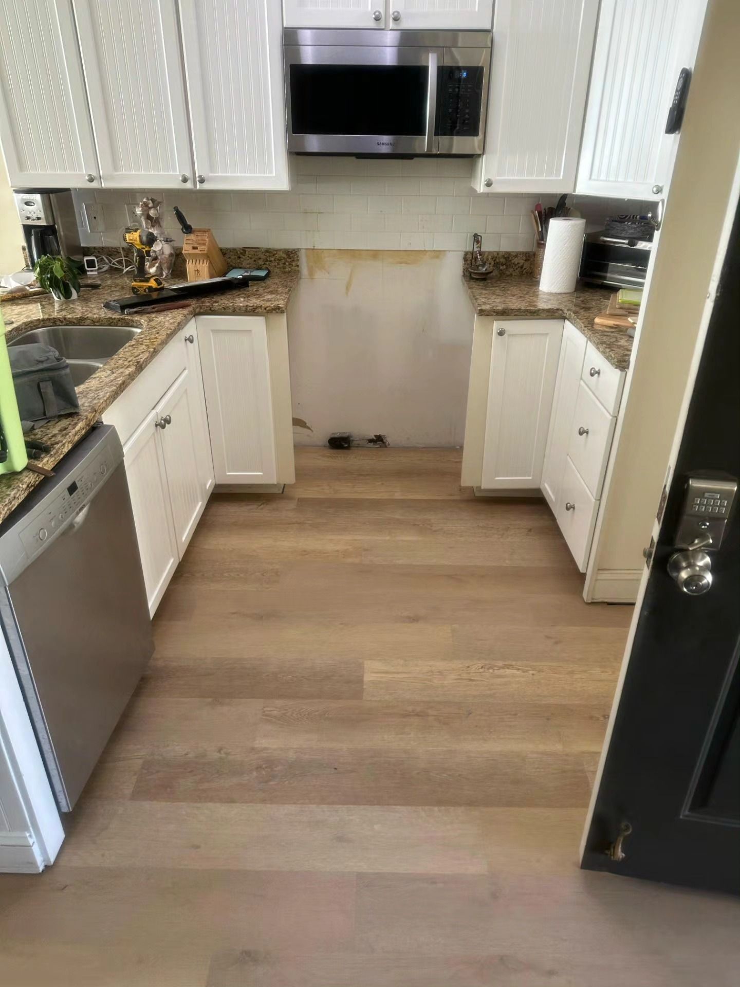 Compact kitchen with white cabinets, stainless appliances, black countertops, and light wood flooring, viewed from the doorway