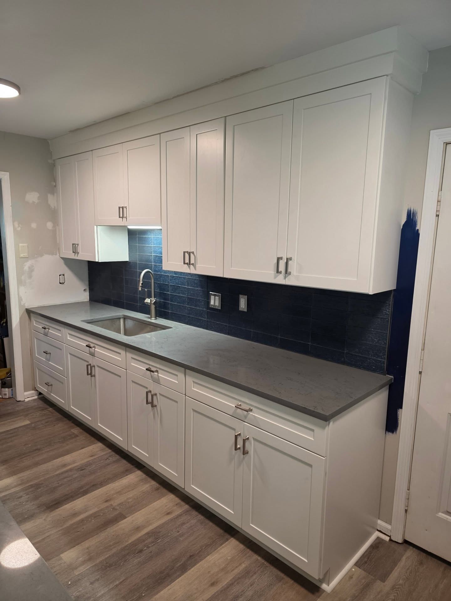 White kitchen cabinets with gray countertops, dark backsplash, and wood-look flooring along one wall.