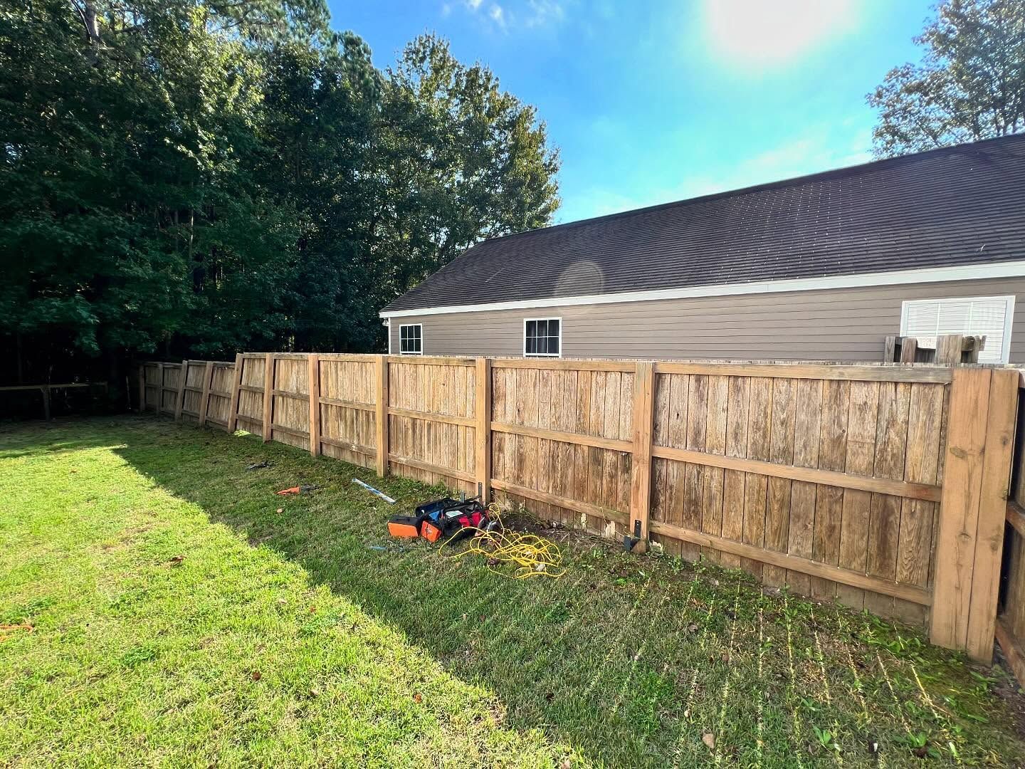 Wooden backyard fence beside a grassy lawn, with a house and trees in the background.