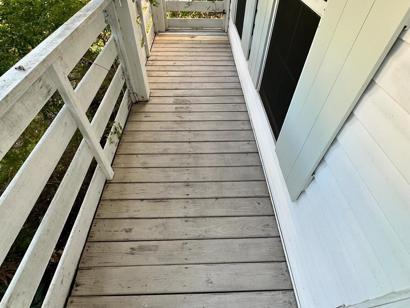 Narrow wooden porch walkway with white railings and house siding in daylight