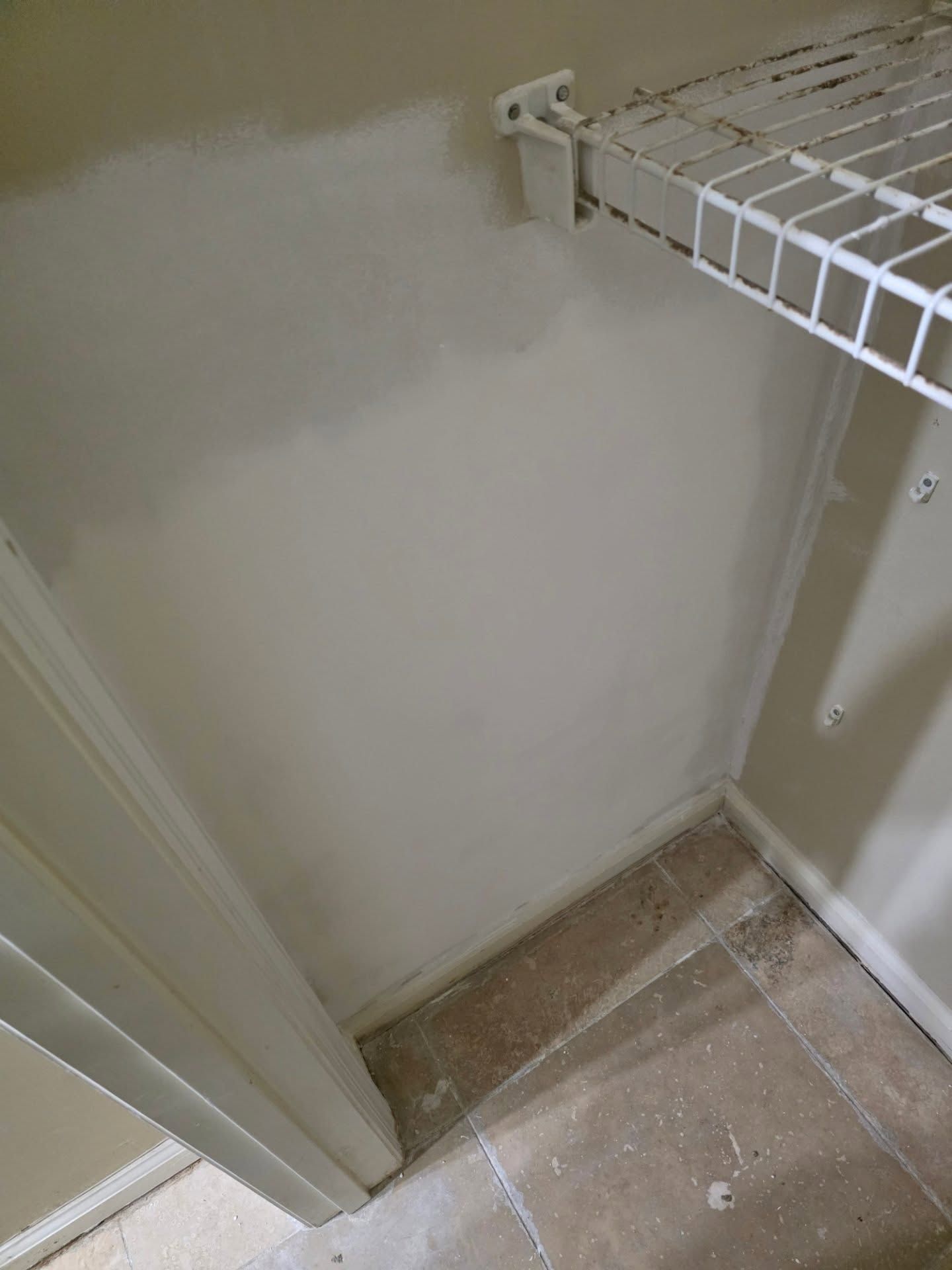 Empty closet corner with white wire shelving, beige walls, and tiled floor