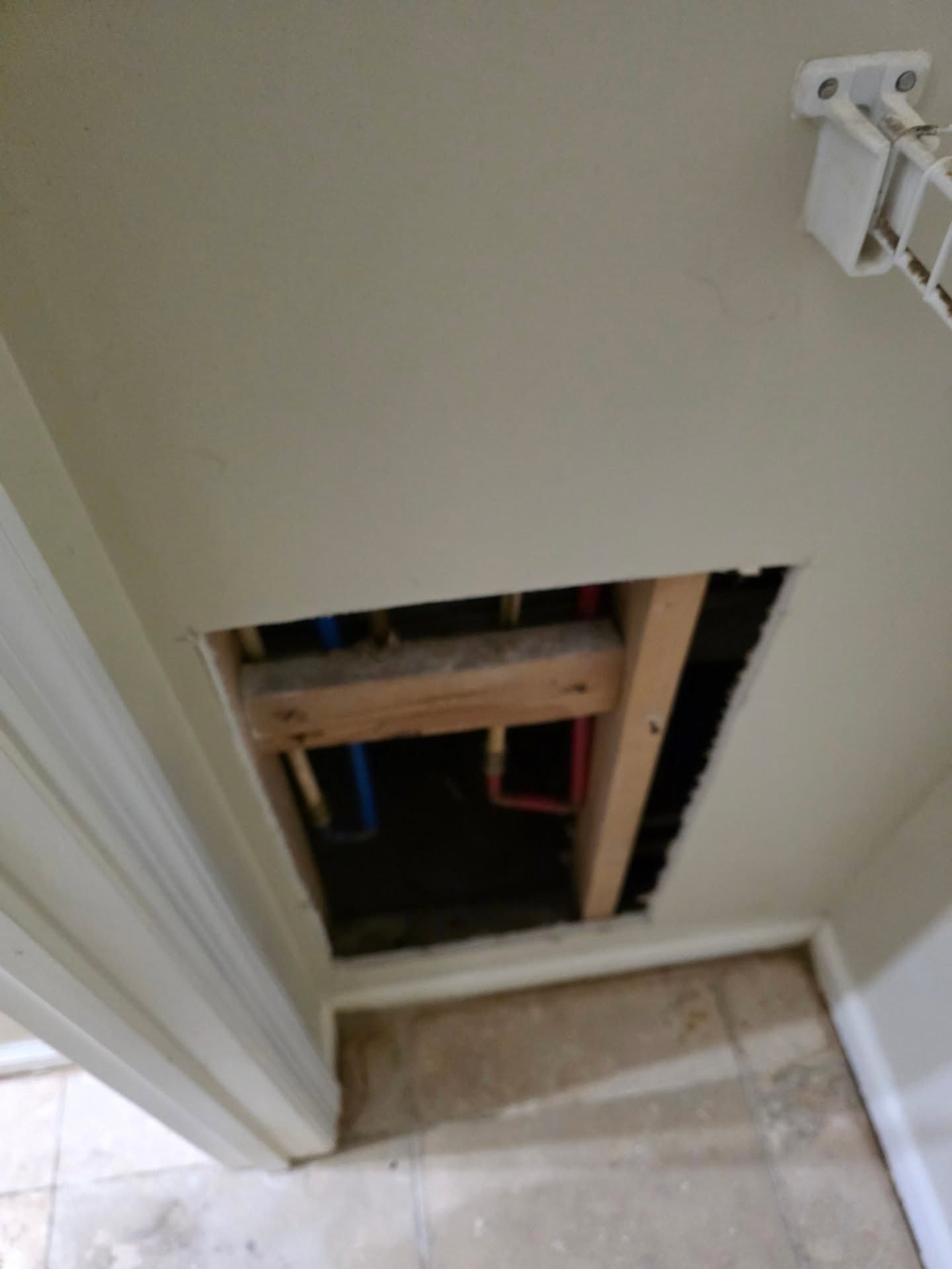 Open wall cavity in a hallway beside a white door and tiled floor