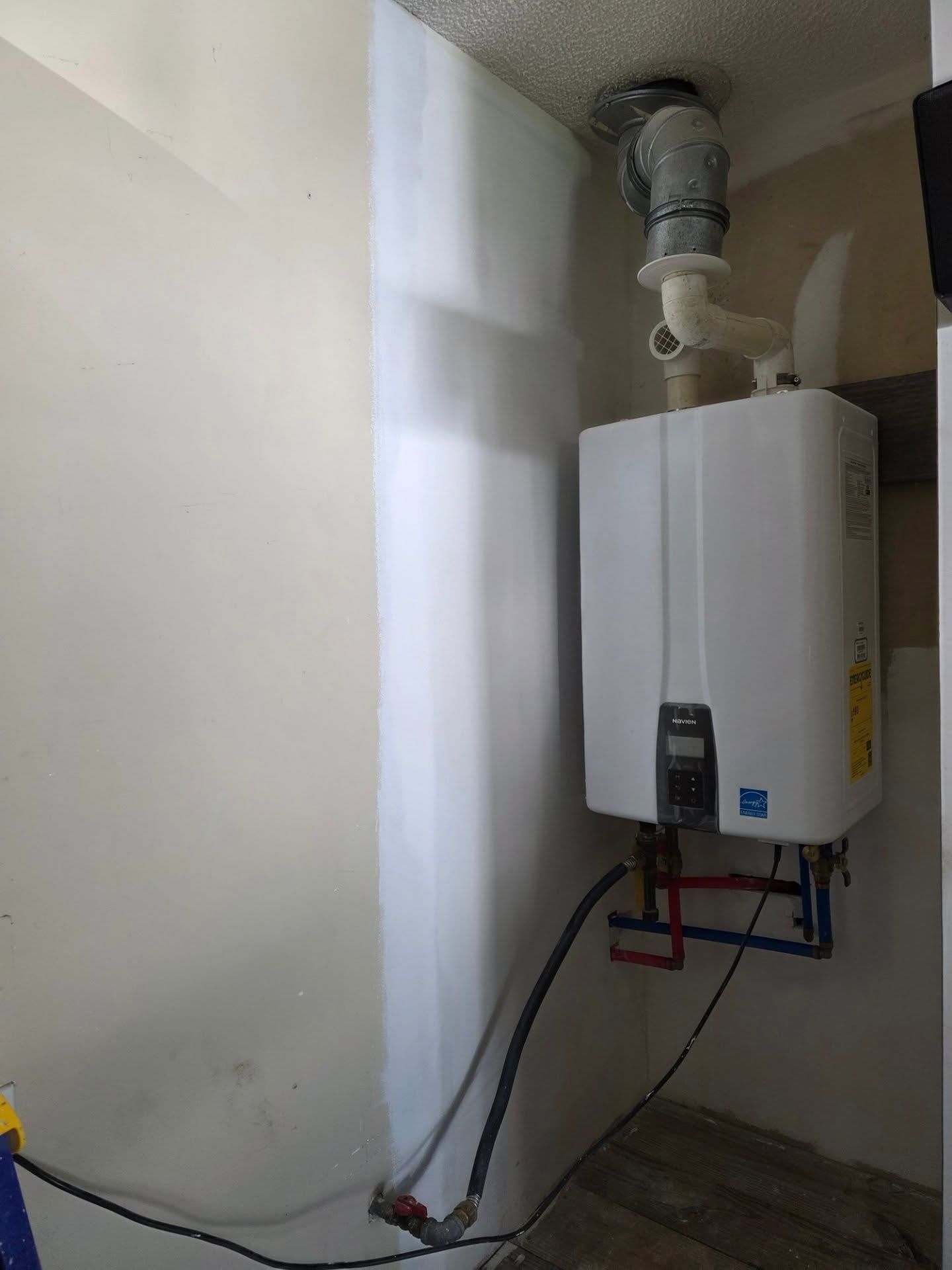 Wall-mounted white water heater with pipes and venting in a small utility room