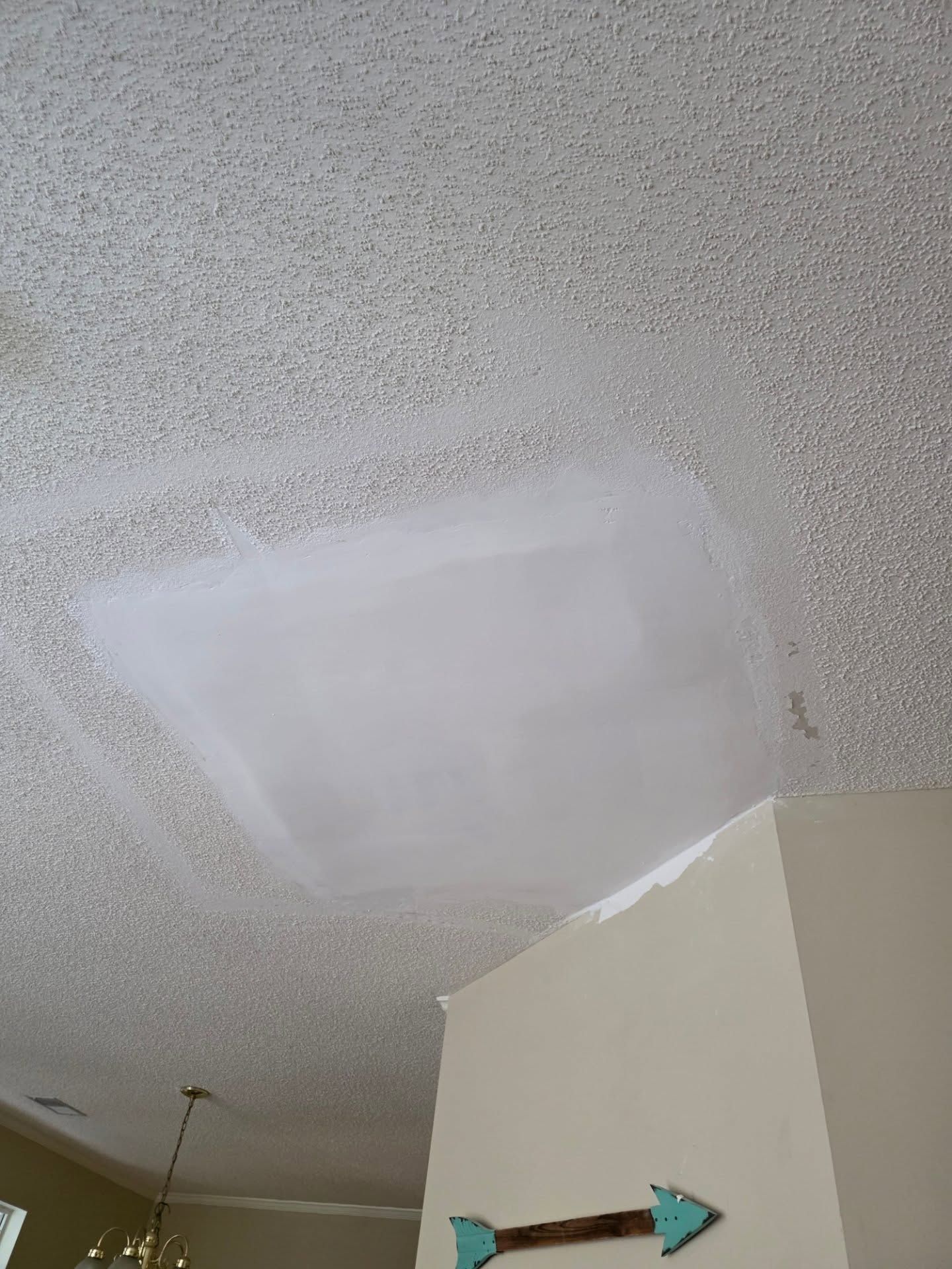 White patch on a textured ceiling above a wall corner in a room