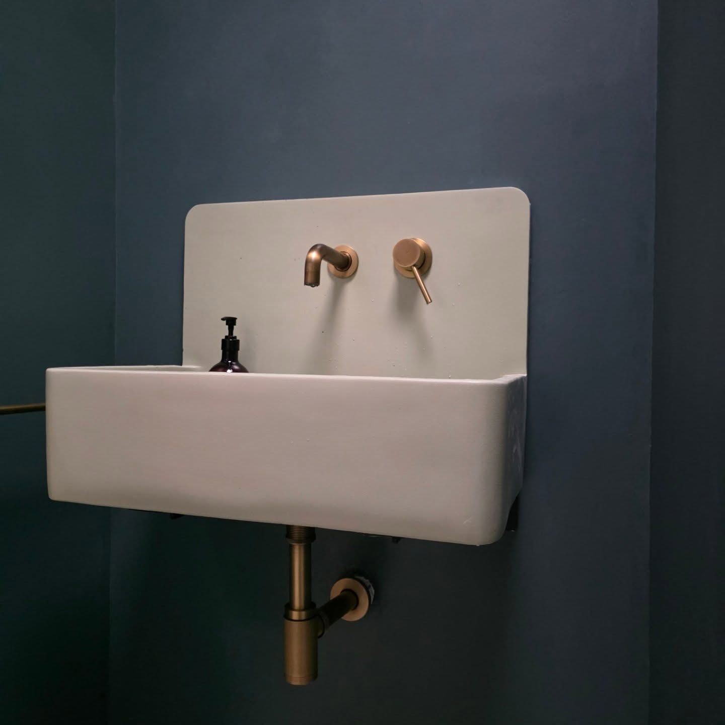 White wall-mounted sink with gold faucets against a dark blue wall