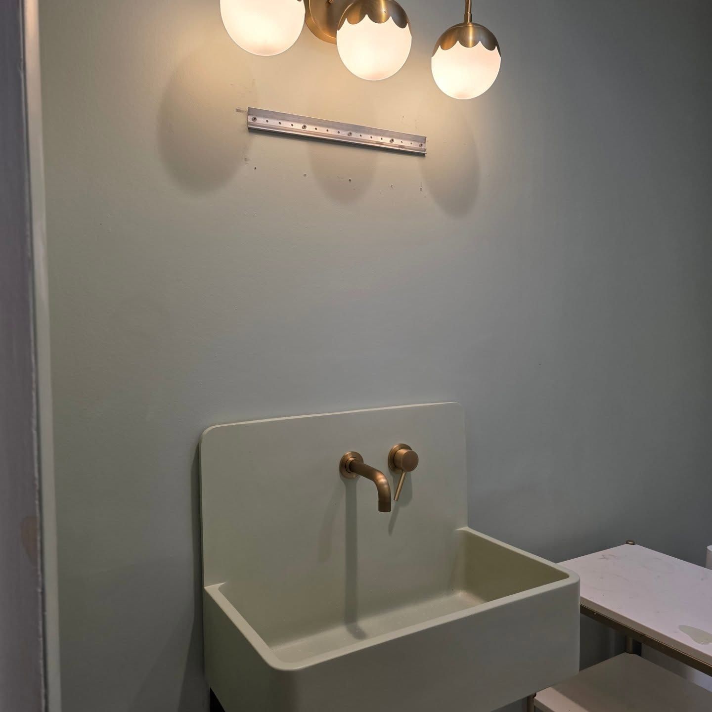 Wall-mounted sink with brass faucet under three globe lights in a small gray bathroom