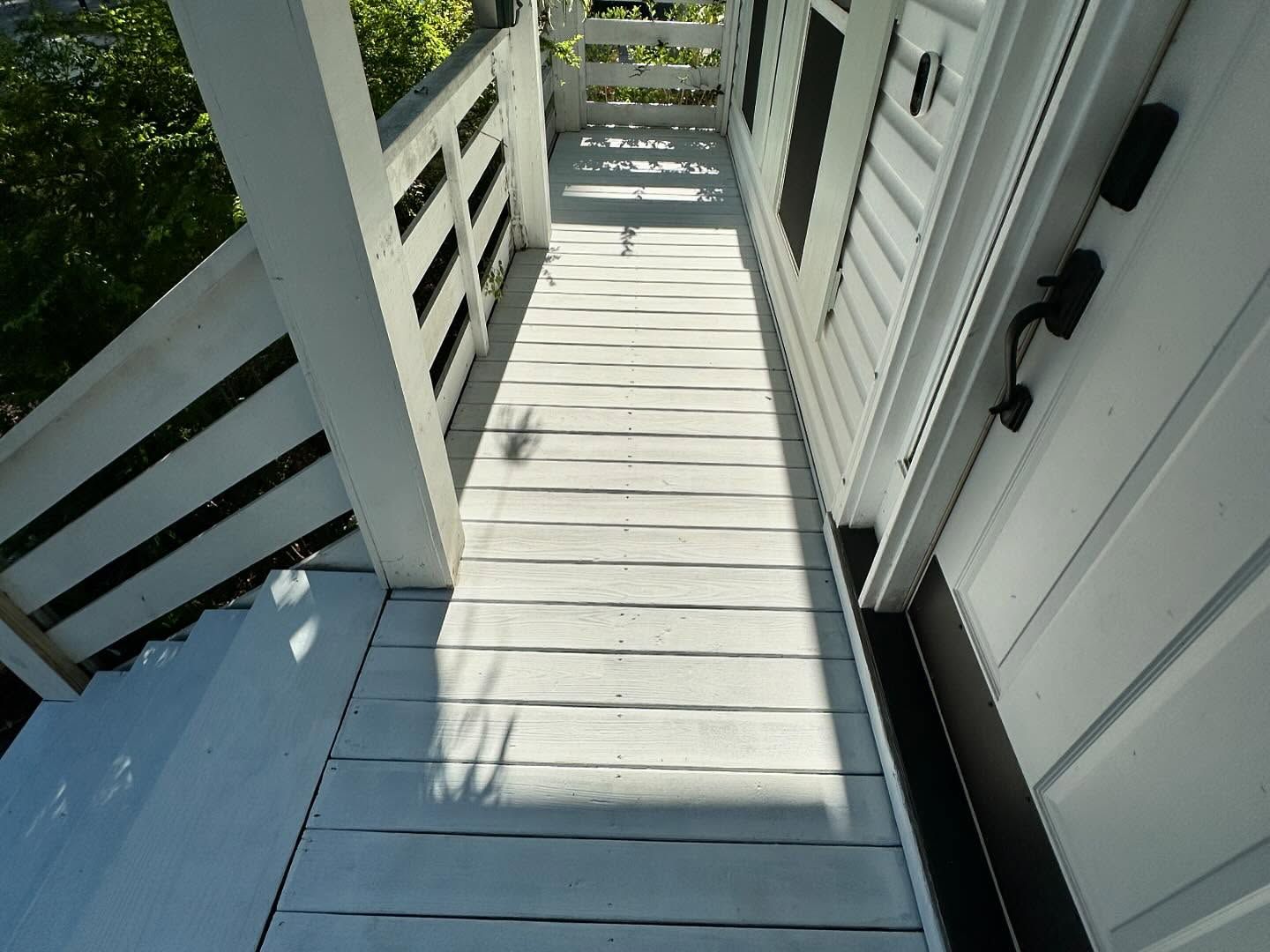 Narrow white porch walkway with railings and sunlight shadows beside a house entrance