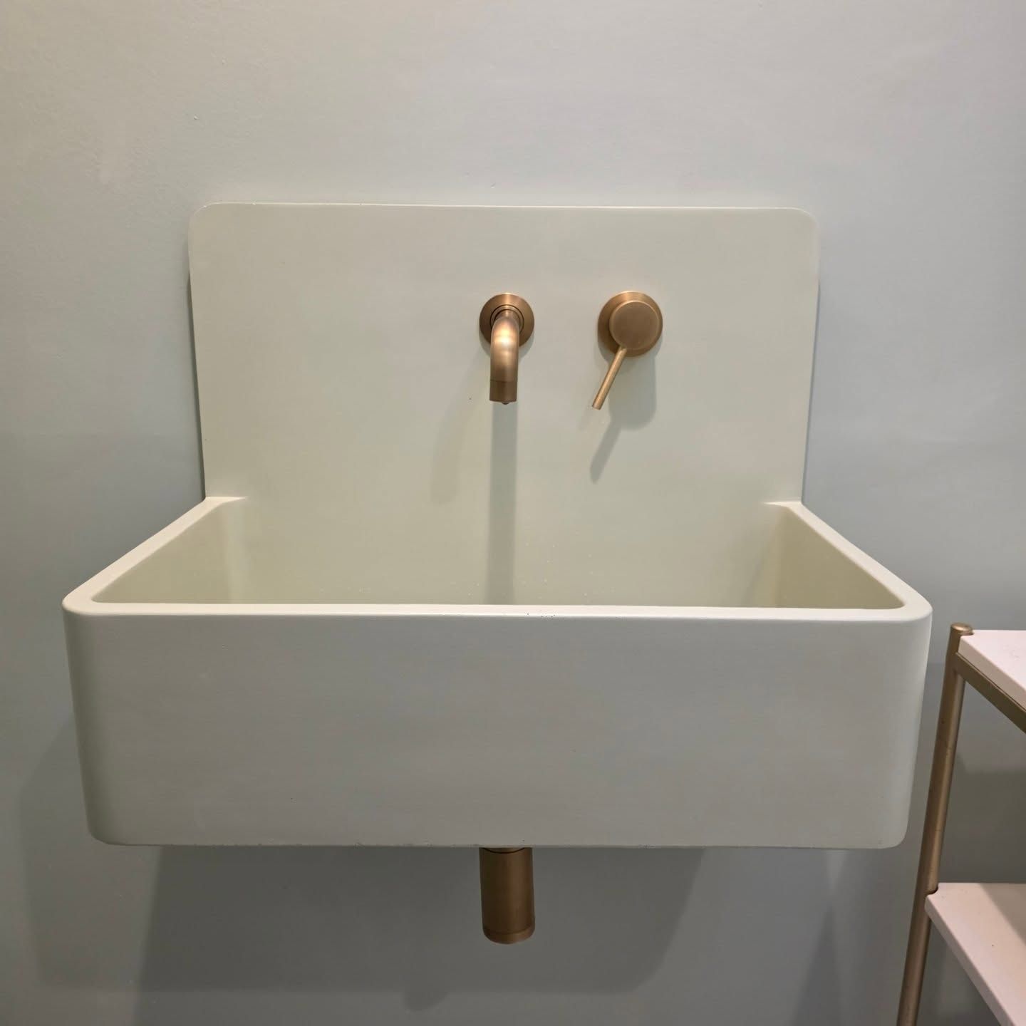 White wall-mounted sink with brass faucet and drain in a minimalist room