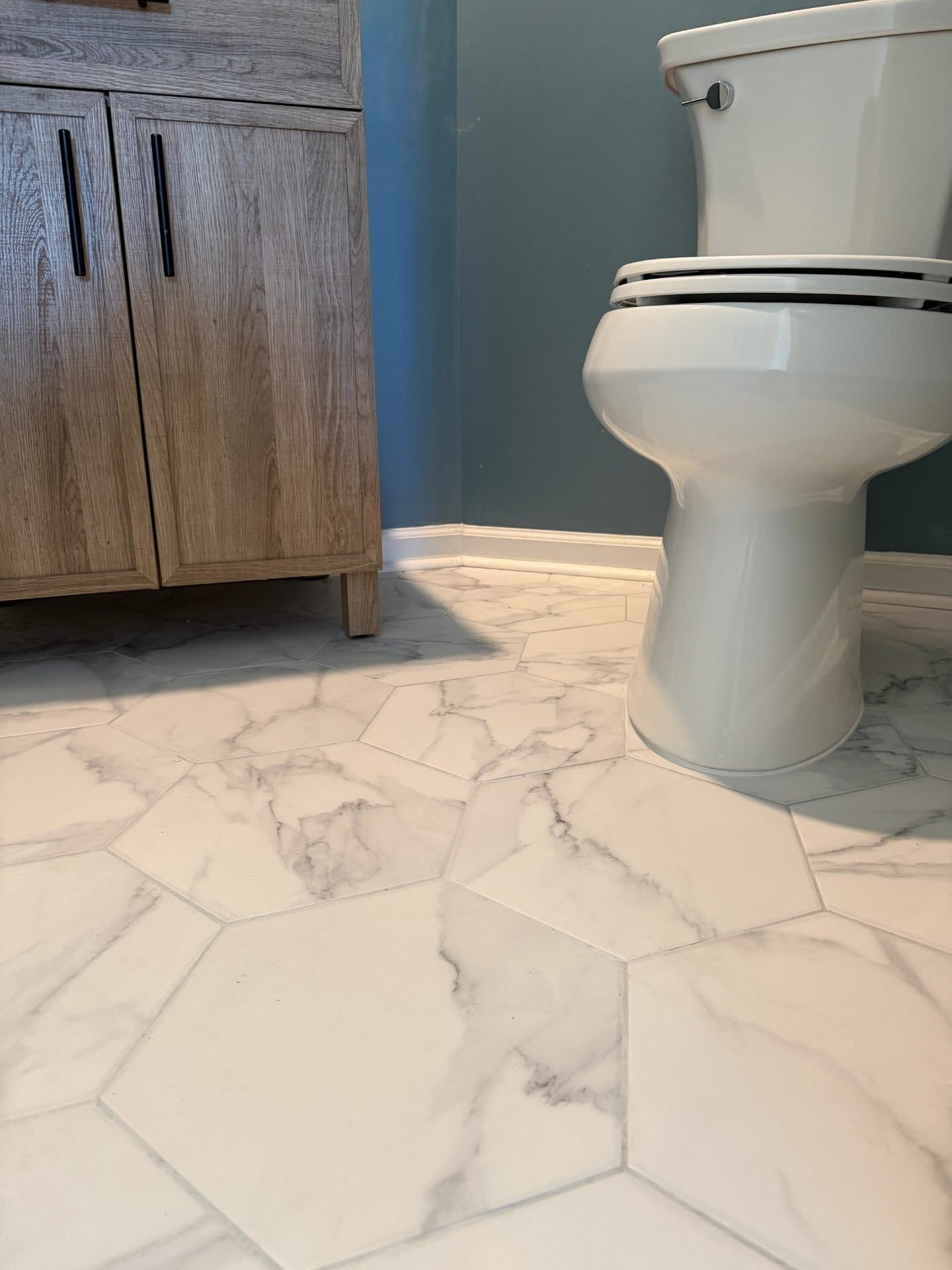 Bathroom with white marble tile floor, wood vanity on the left, and a white toilet on the right.