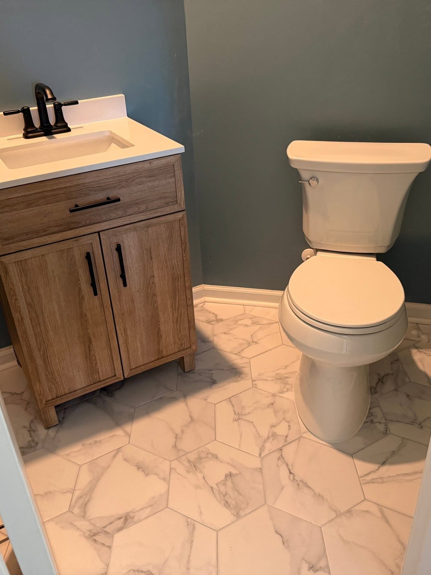 Bathroom with white vanity and toilet, marble-pattern tile floor, and blue-gray walls.