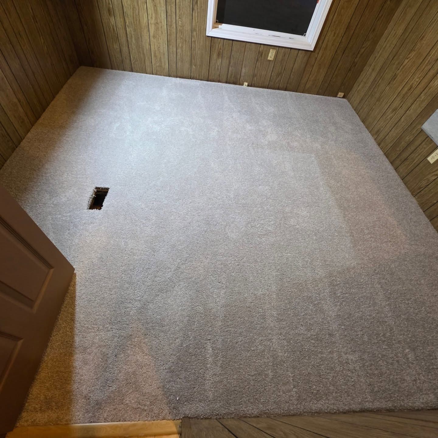Empty carpeted room with wood-paneled walls, a small window, and a floor vent.