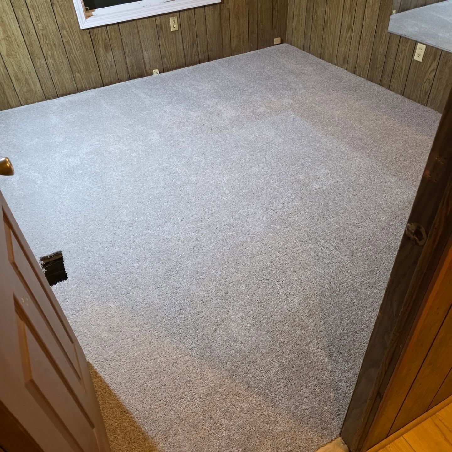 Empty room with light gray carpet, wood-paneled walls, and an open door in the foreground