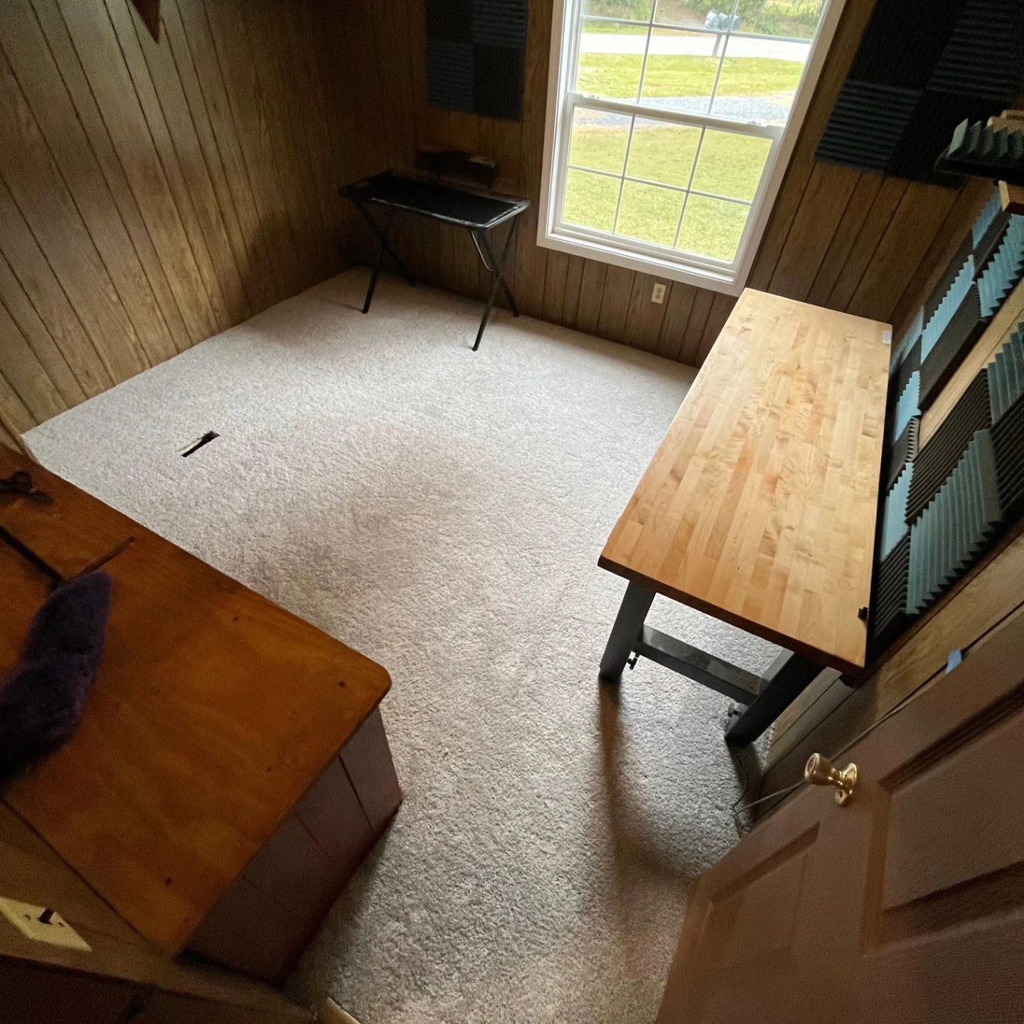 Small wood-paneled room with a bed, desk by a window, and carpeted floor.