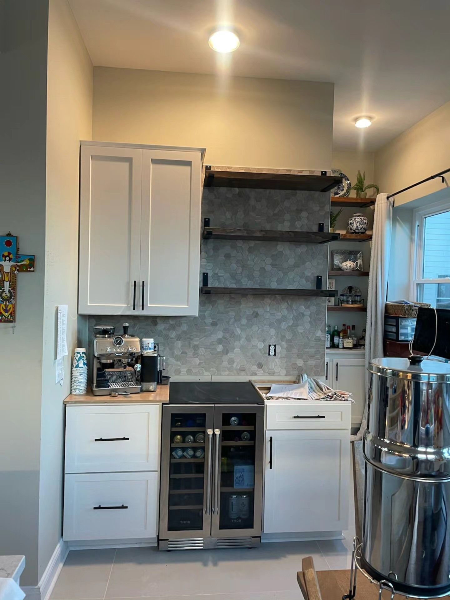 Small kitchen with white cabinets, open shelves, and a stainless steel refrigerator next to a window.
