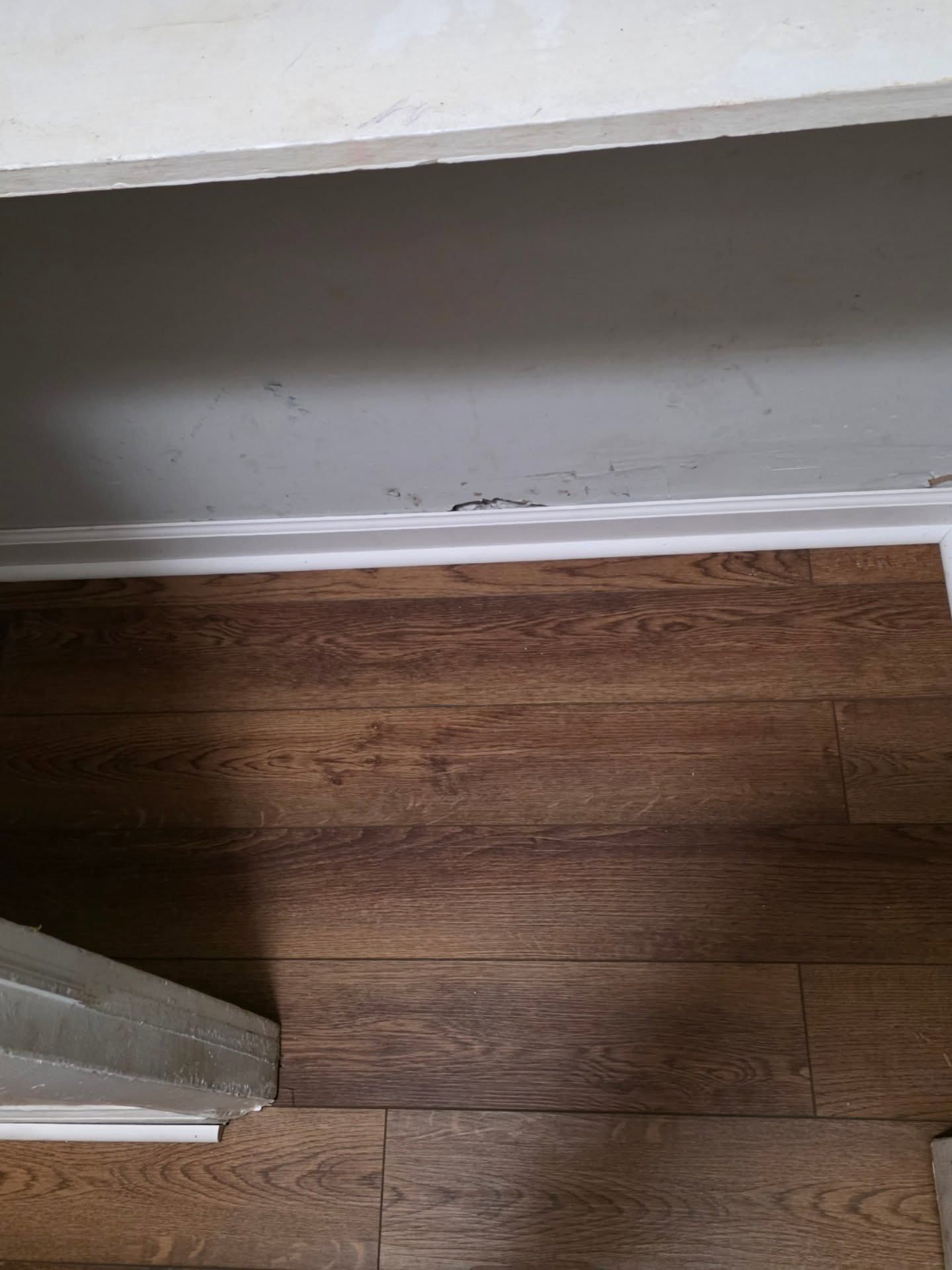 Brown wood floor beside a white wall with scuff marks and a doorframe corner