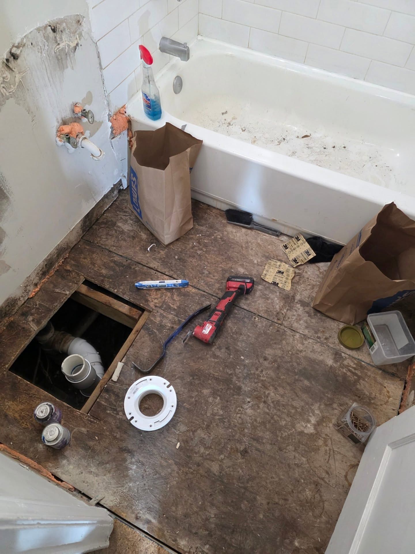 Dirty bathroom floor with scattered tools and debris near an open toilet access hole