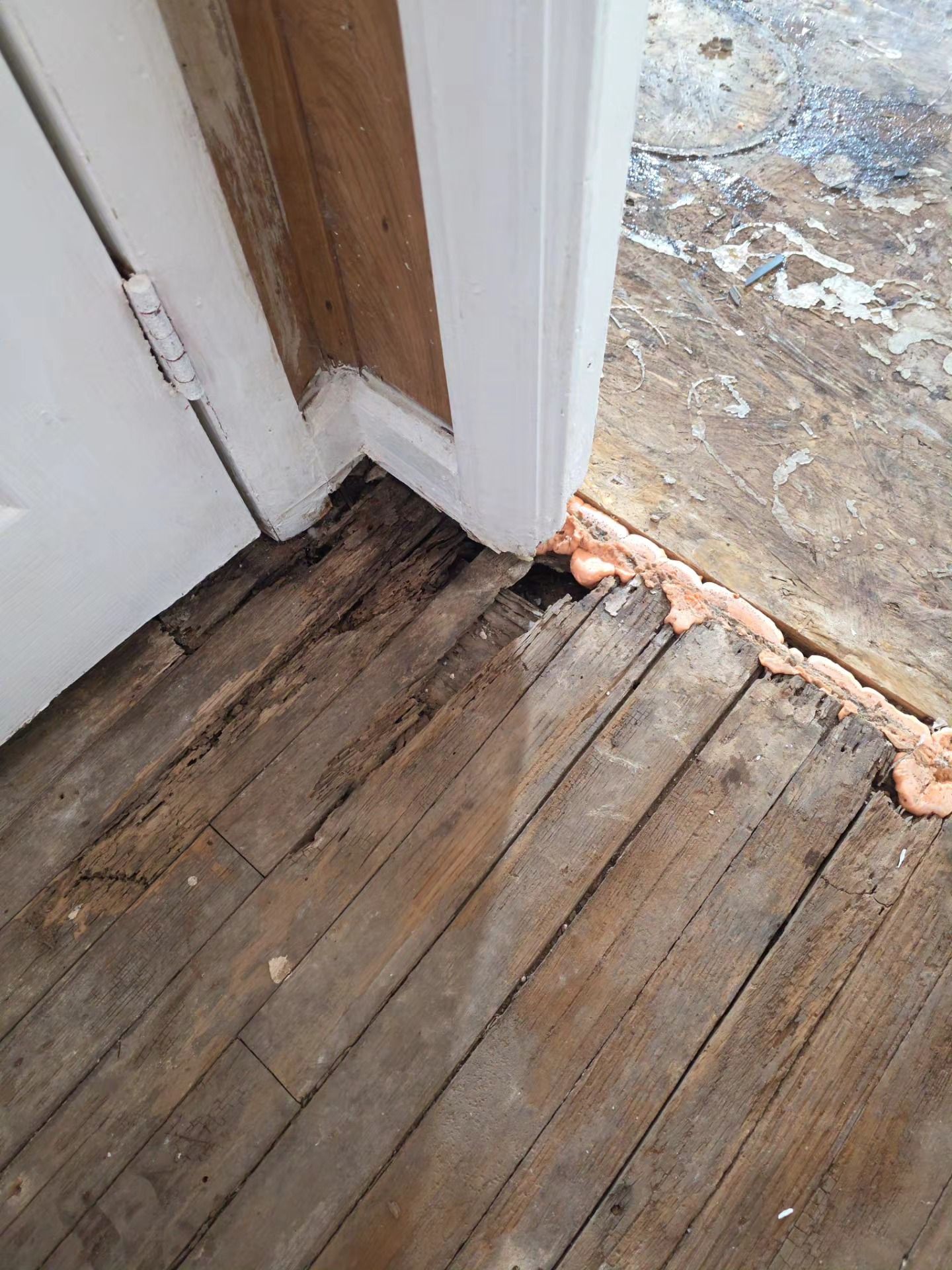 Damaged wooden floor at a doorway with a visible gap to the outside ground