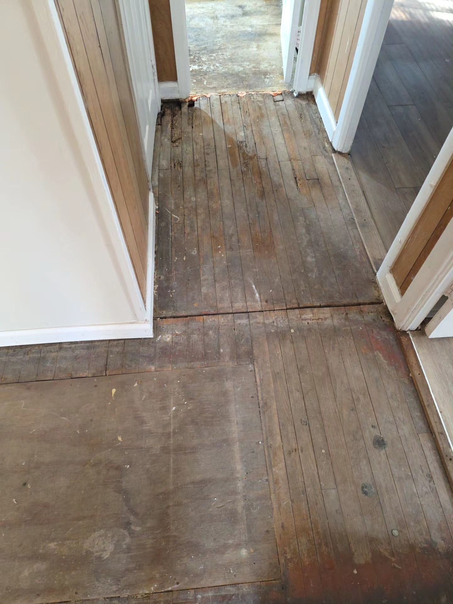 Water-damaged hallway floor with peeling, stained boards near doorways