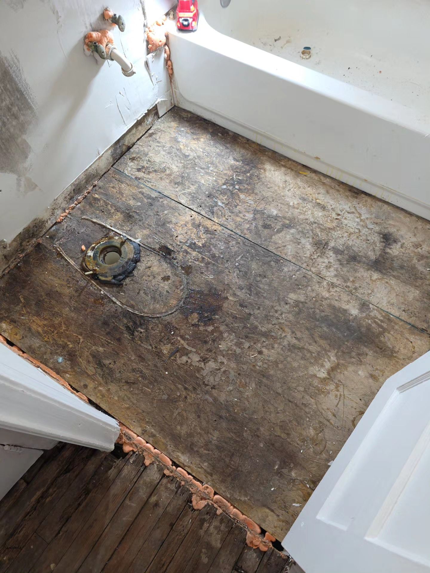 Small bathroom with subfloor exposed, missing flooring, and a toilet flange visible near the doorway.