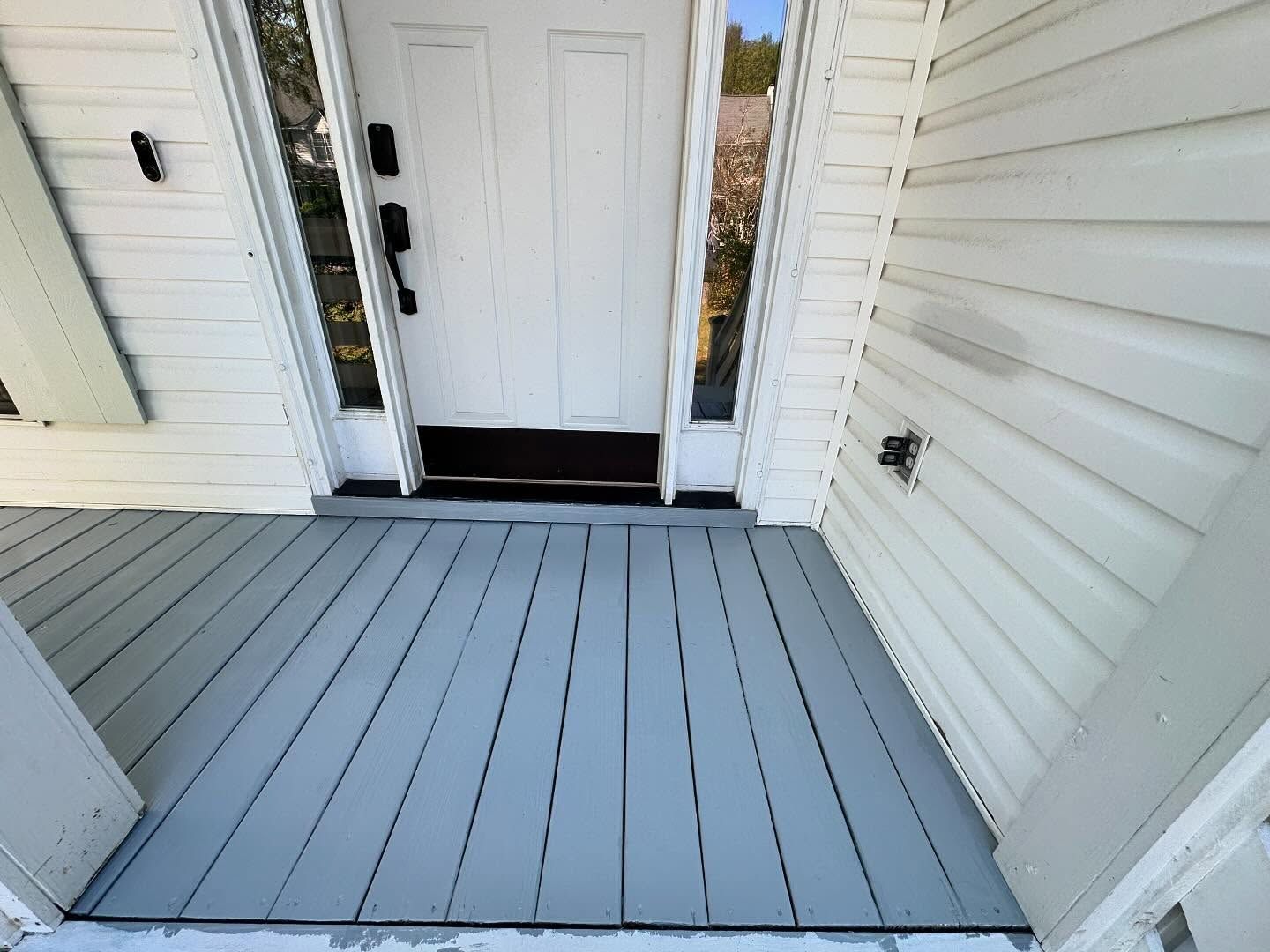 Front porch with gray flooring, white siding, and a white front door.