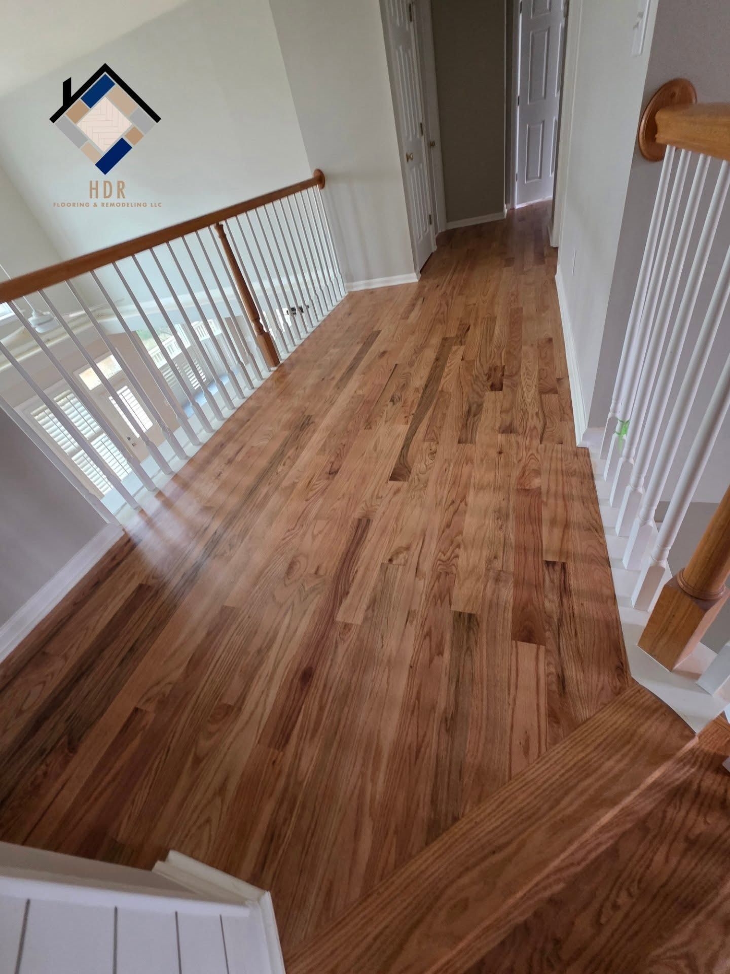 Wooden hallway with white railings and a staircase landing, viewed from above.