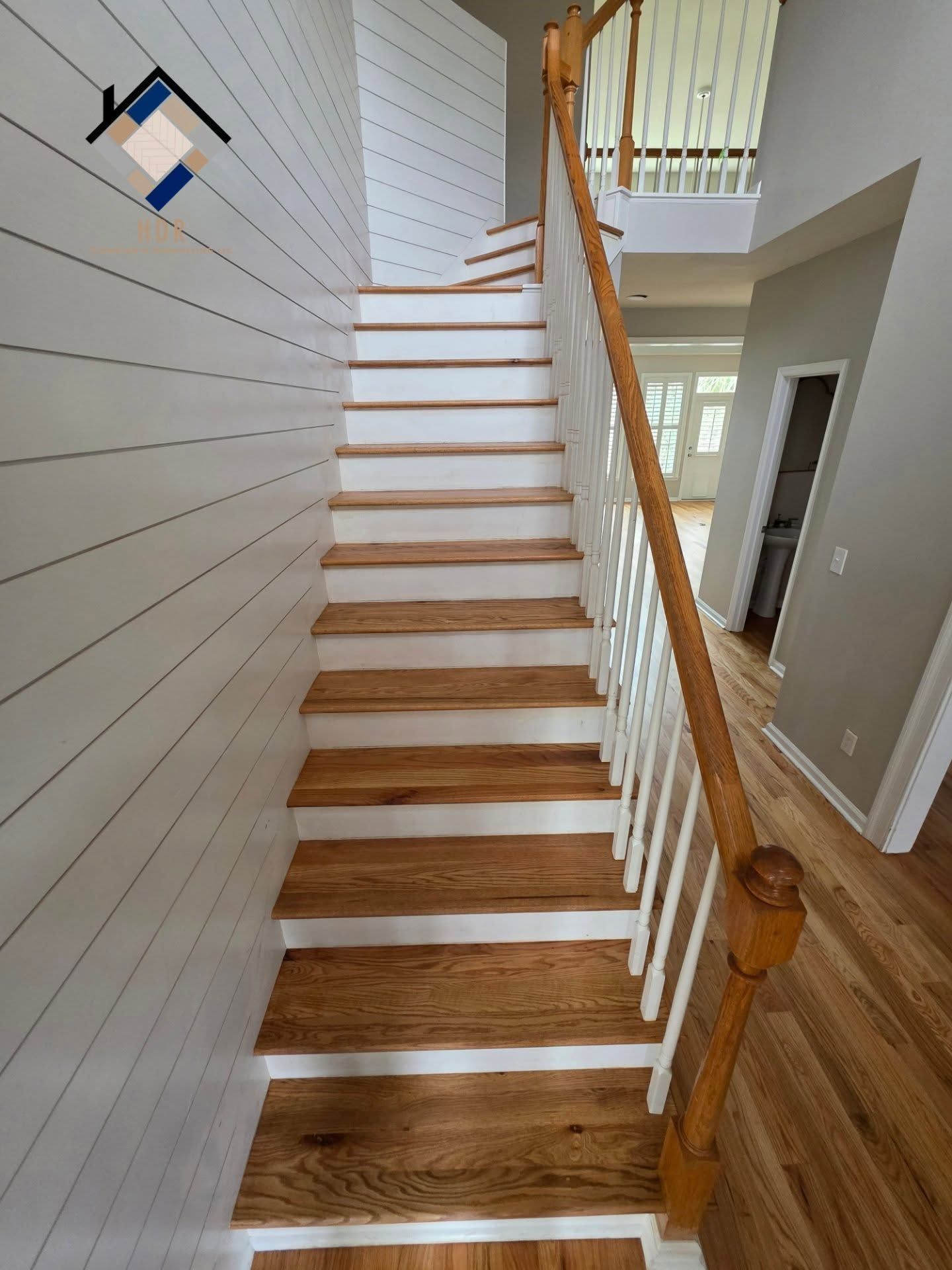 Interior staircase with white walls, wood steps, and a wooden handrail in a bright hallway
