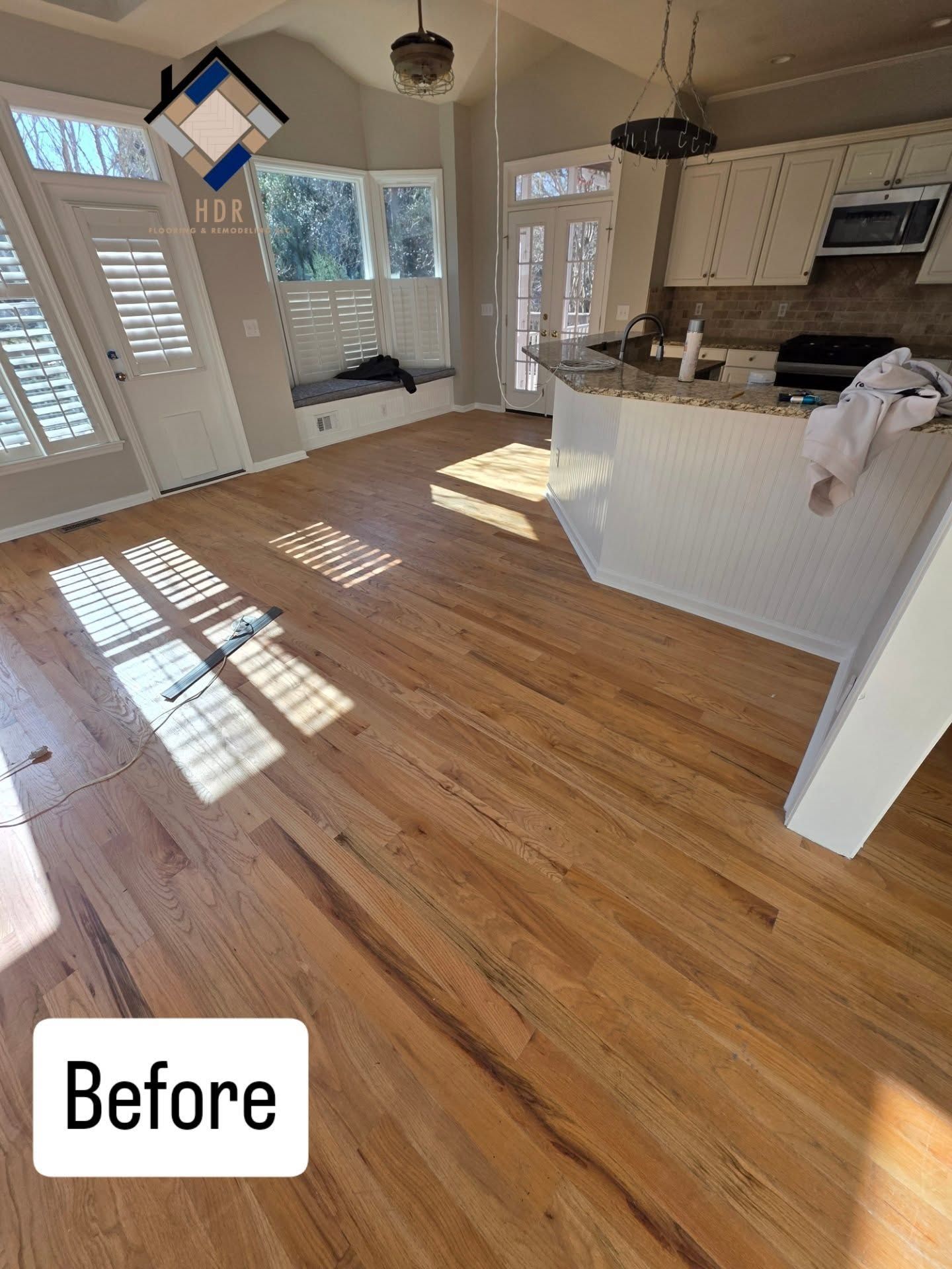 Empty kitchen with wood floors, white cabinets, and bright sunlight streaming through the windows.