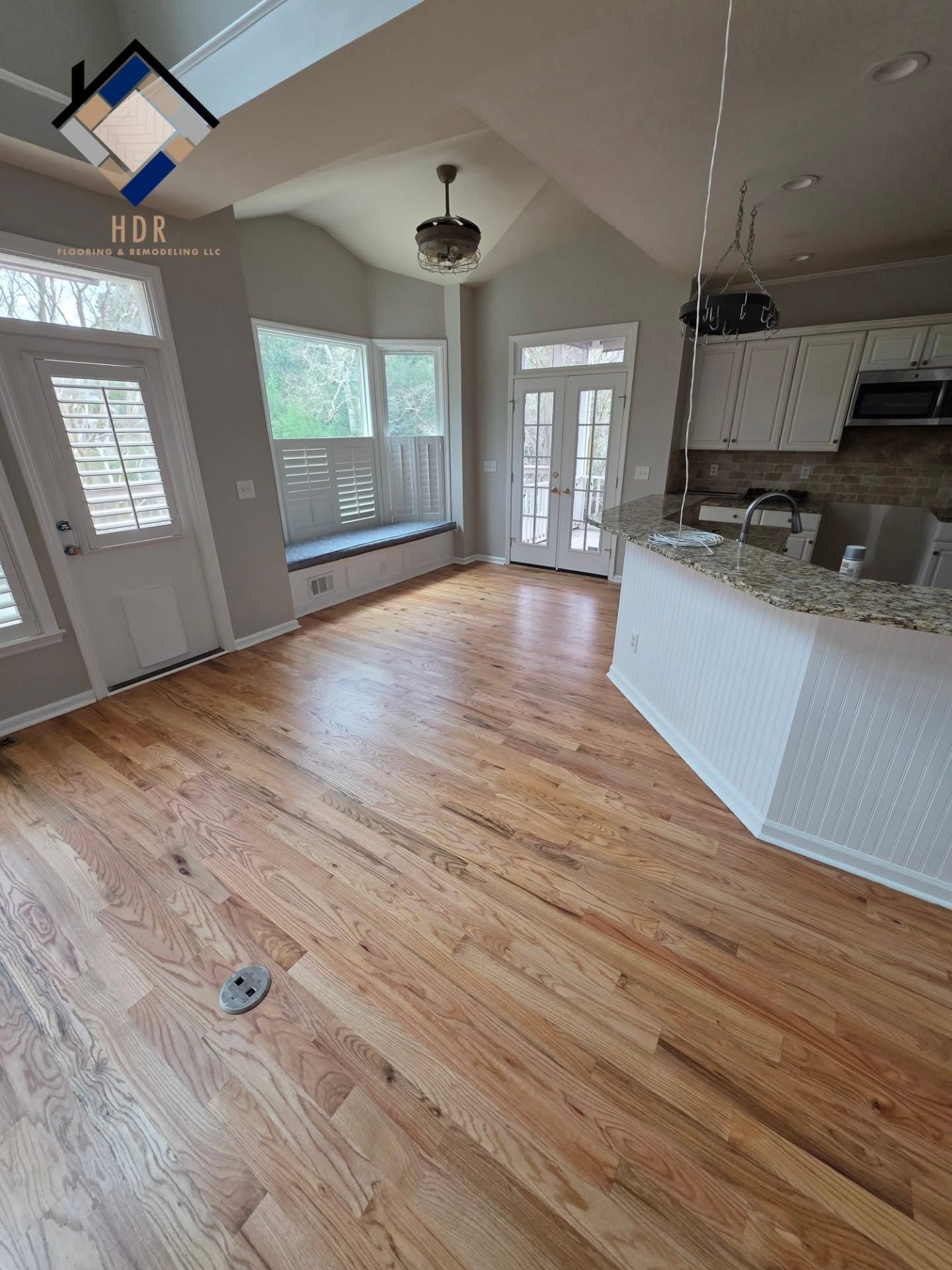 Empty kitchen and dining area with hardwood floors, white cabinets, and large windows.