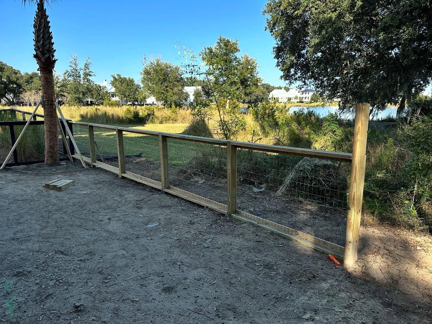 Wooden fence beside a gravel path overlooking a grassy field under trees in bright sunlight