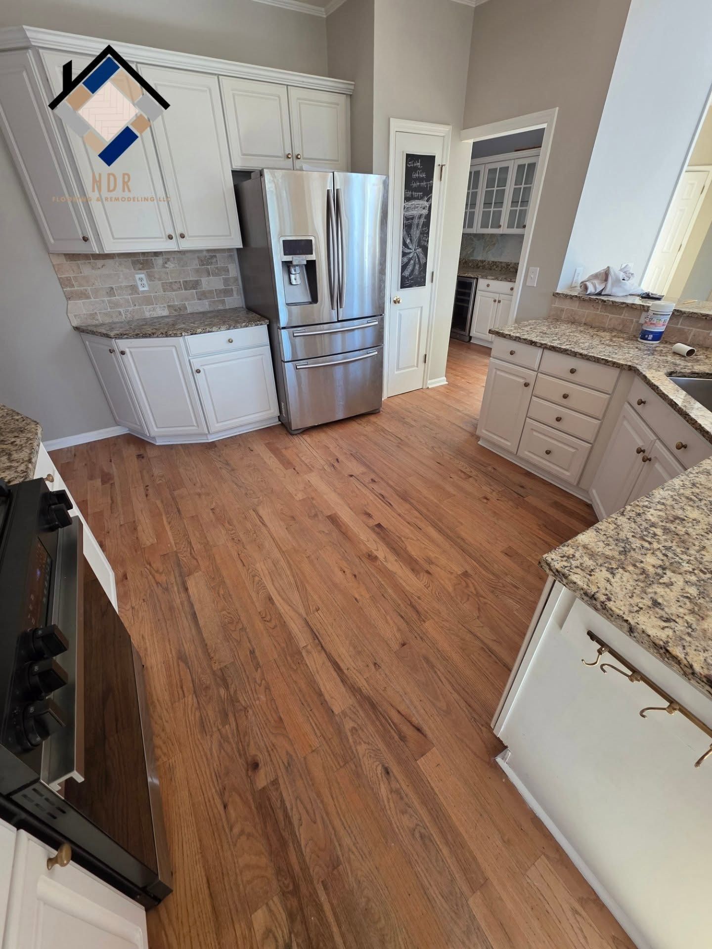 Modern kitchen with stainless steel fridge, white cabinets, granite counters, and hardwood floors