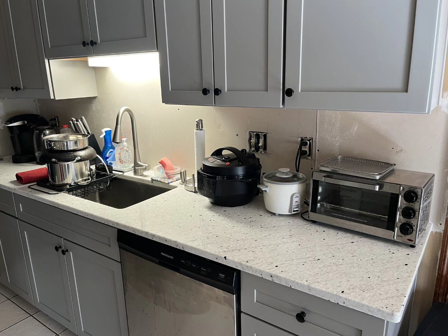 Kitchen counter with sink, black appliances, and a toaster oven under gray cabinets.