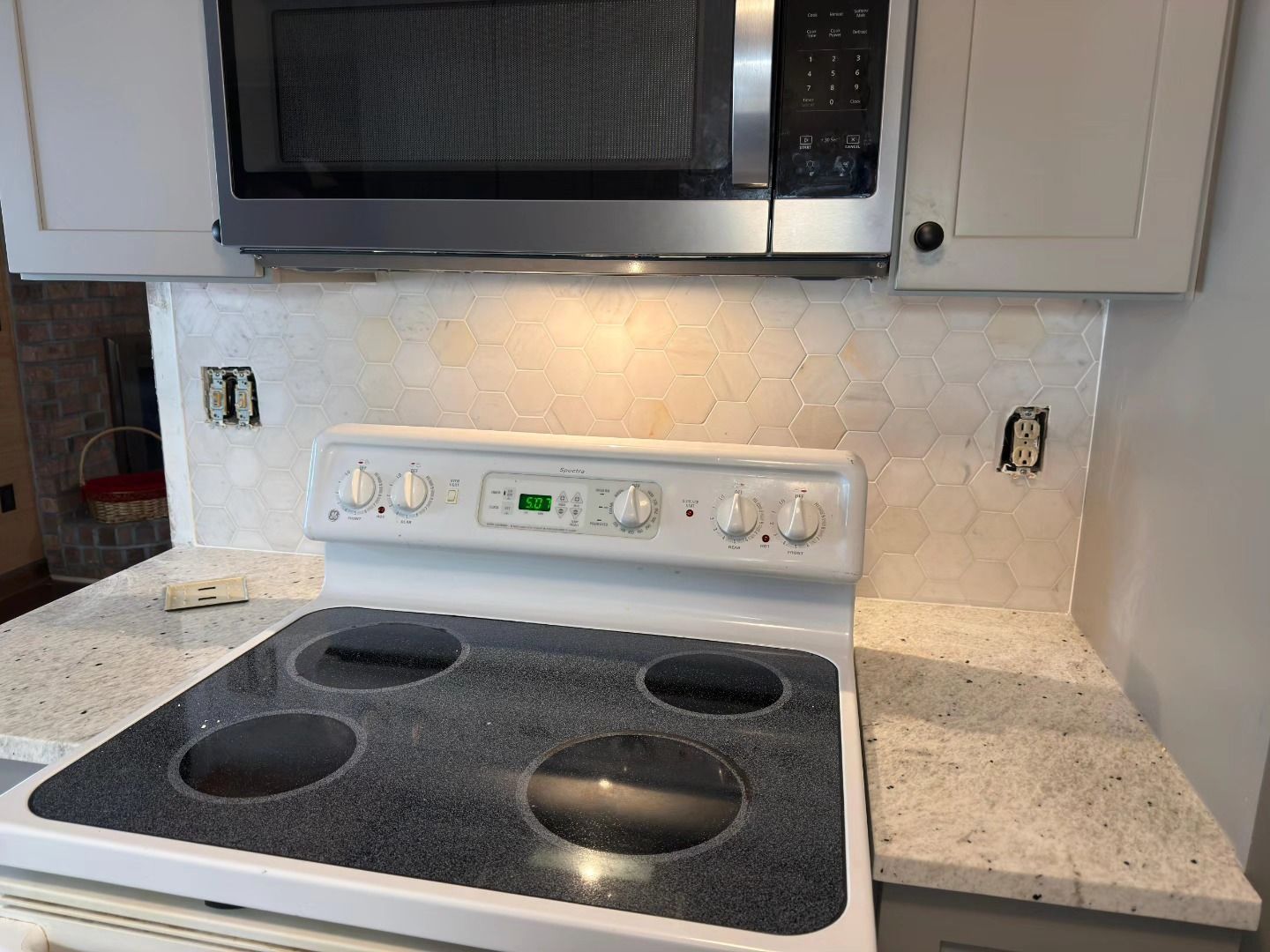White kitchen stove and microwave built into cabinets with granite countertop and black cooktop.