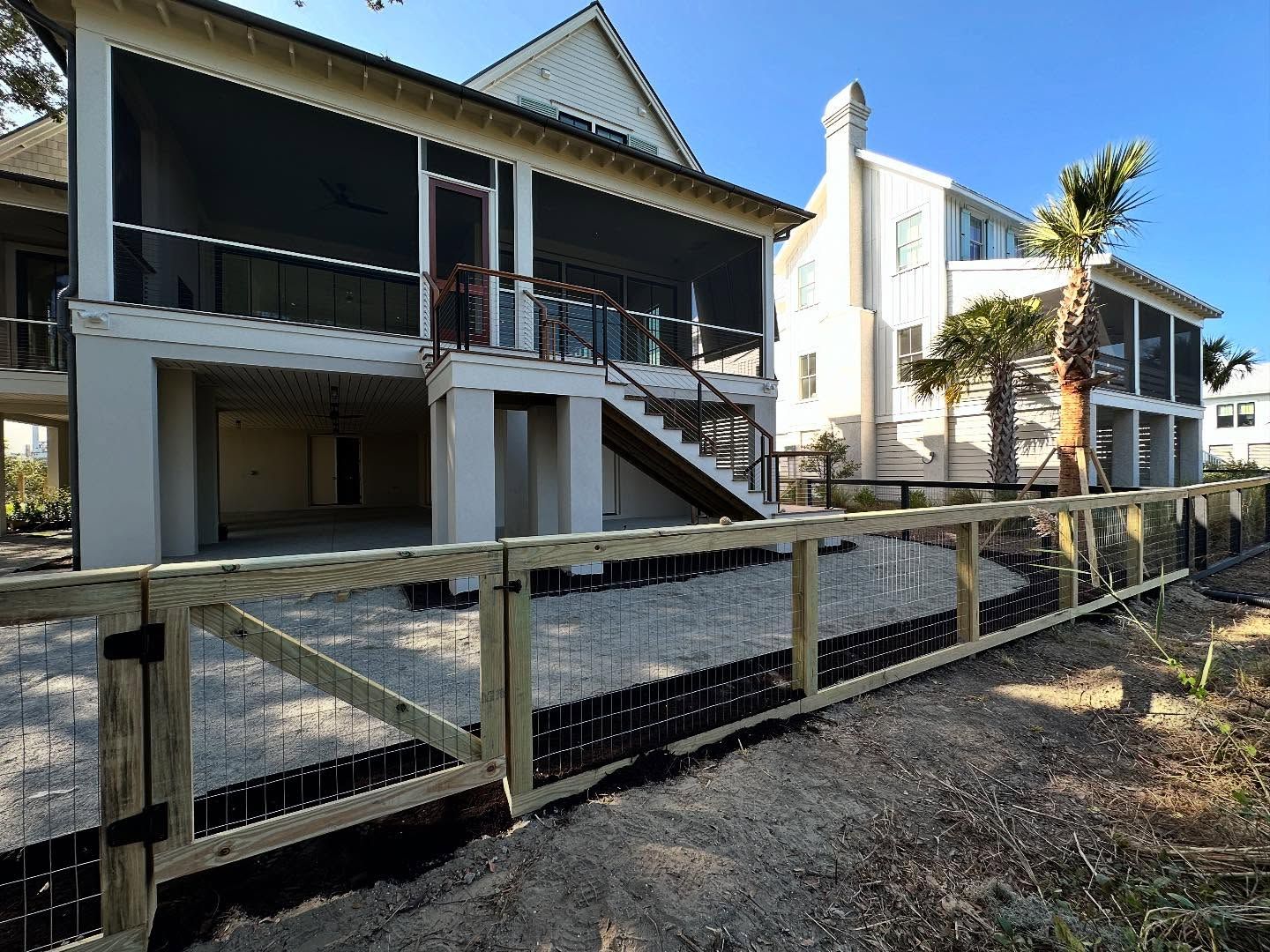 Two-story white houses with balconies behind a wooden fence on a sunny street