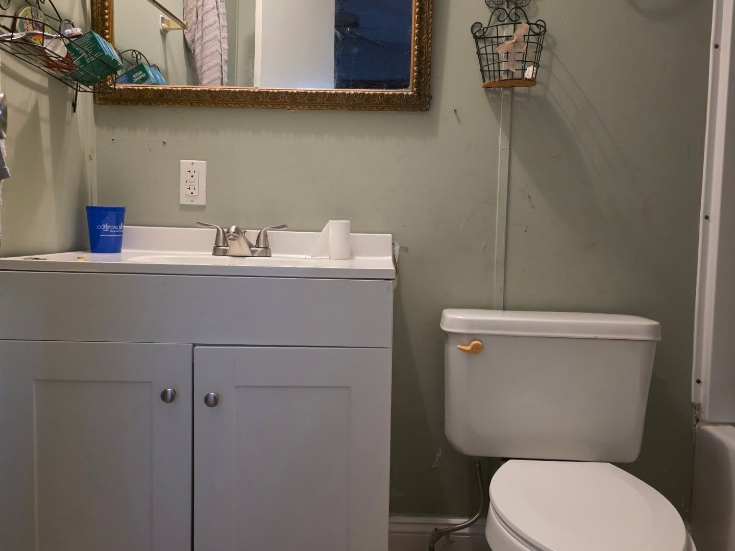Small bathroom with white vanity, mirror, toilet, and a blue cup on the sink.