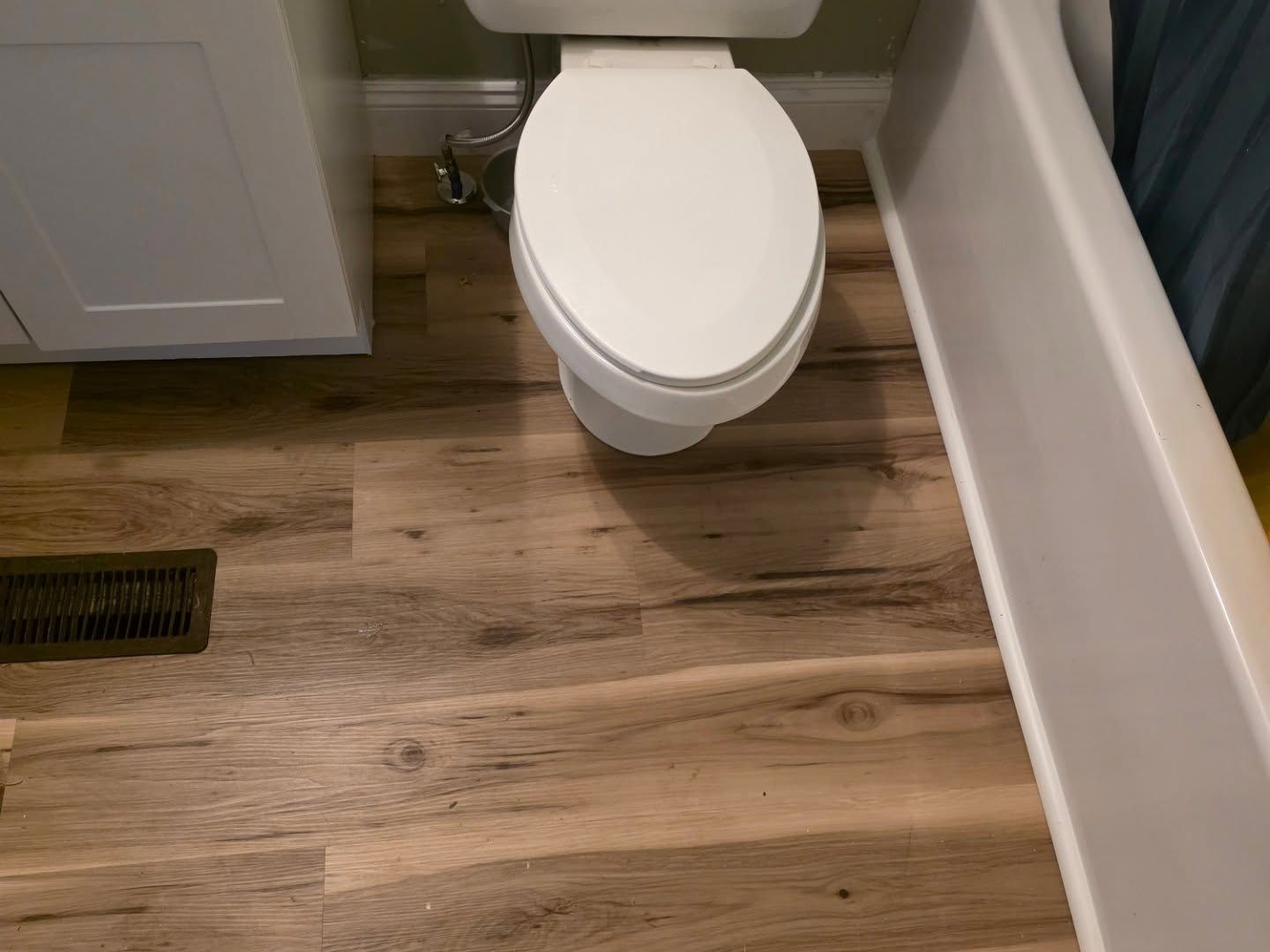 Bathroom with a white toilet, wood-look floor, bathtub edge, and floor vent.