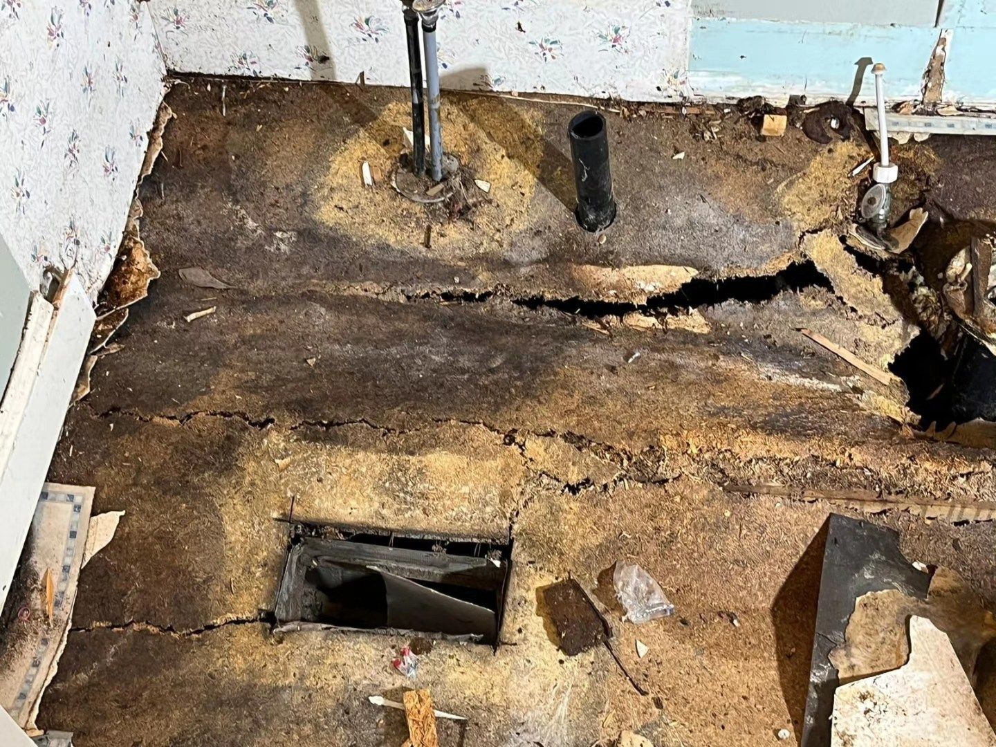 Severely water-damaged floor with rotted wood, exposed subfloor, and broken openings in a room.