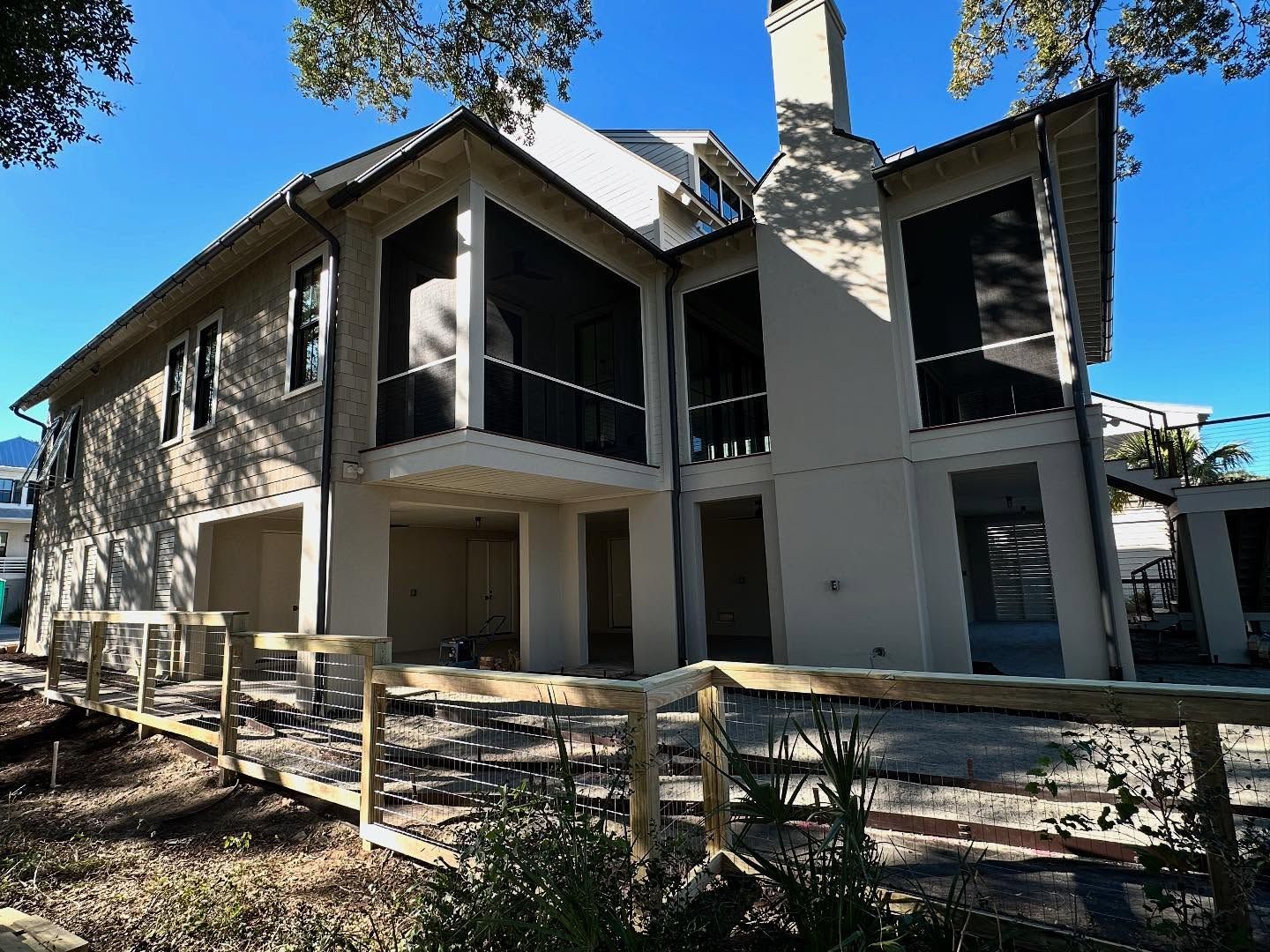Two-story building with balconies and stairs, surrounded by a wooden fence under a clear blue sky