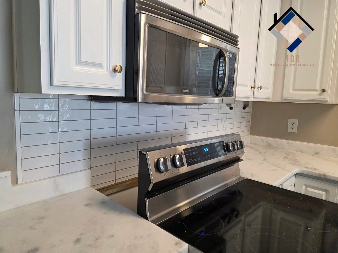 Modern white kitchen with stainless steel microwave and stove, marble countertop, and tiled backsplash