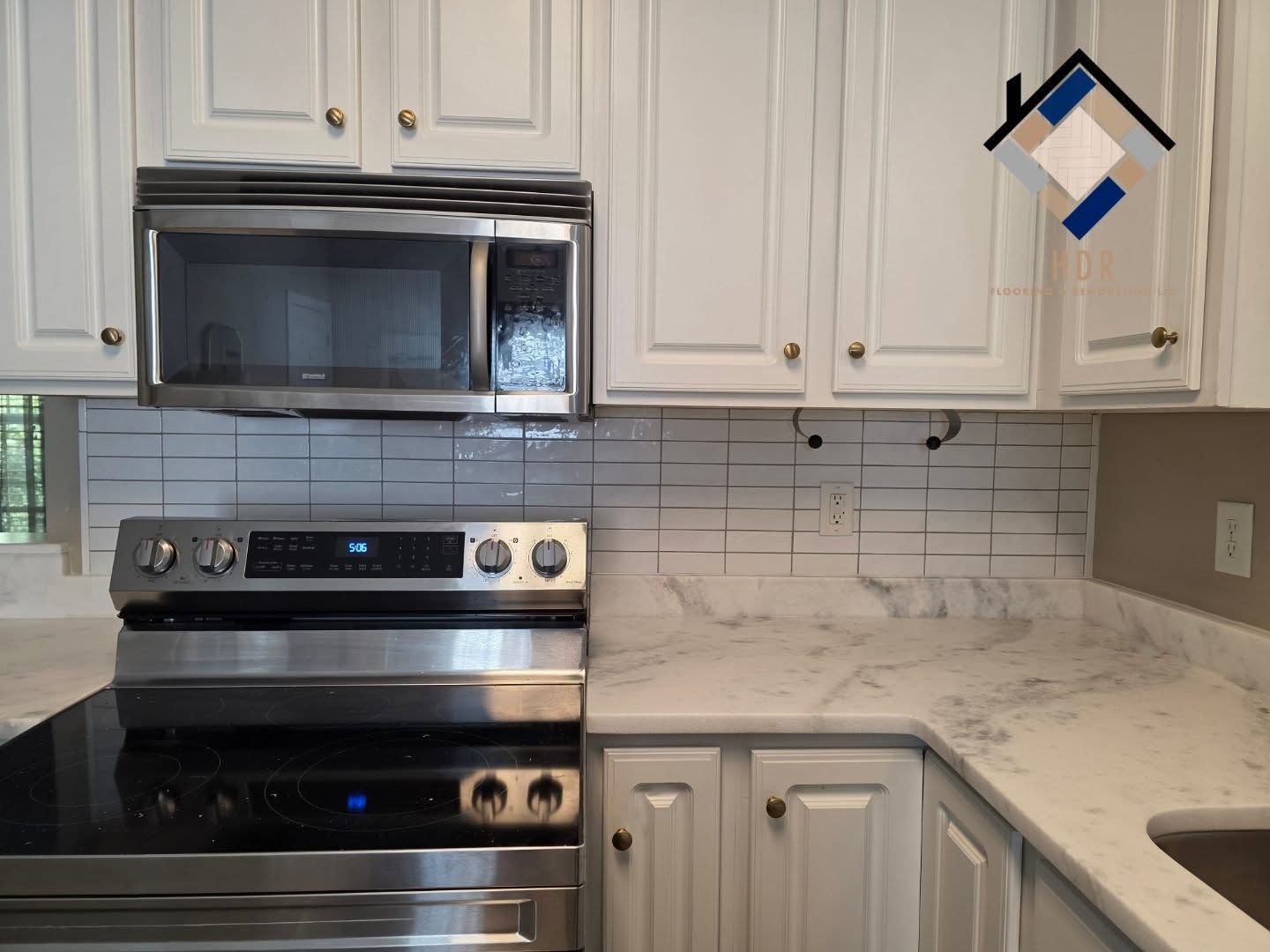 White kitchen with stainless steel stove, microwave, cabinets, and marble-look countertops