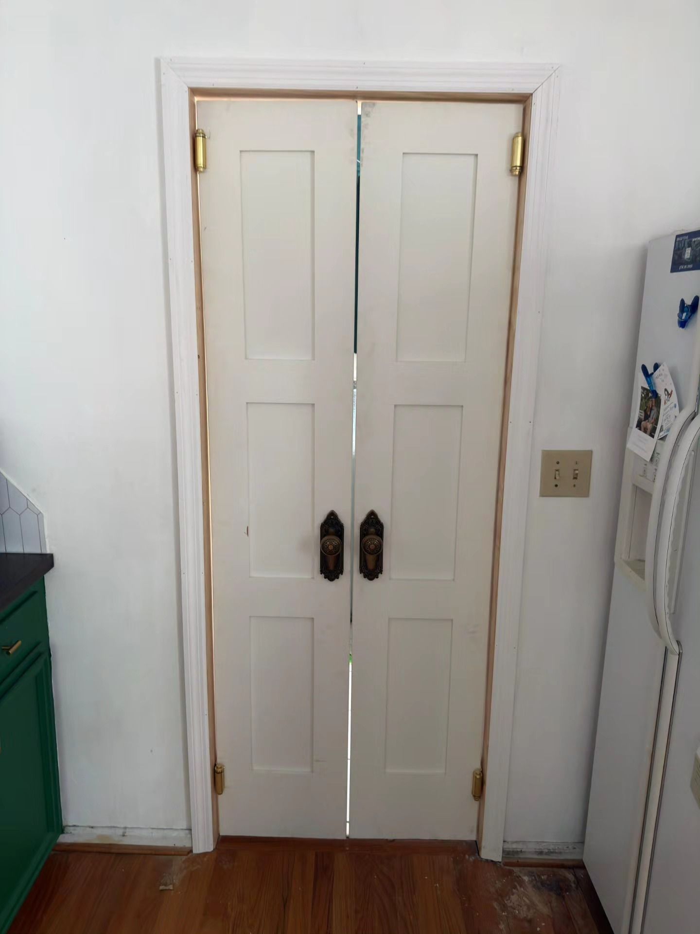 White double closet doors with dark handles in a hallway beside a green cabinet and wall switches