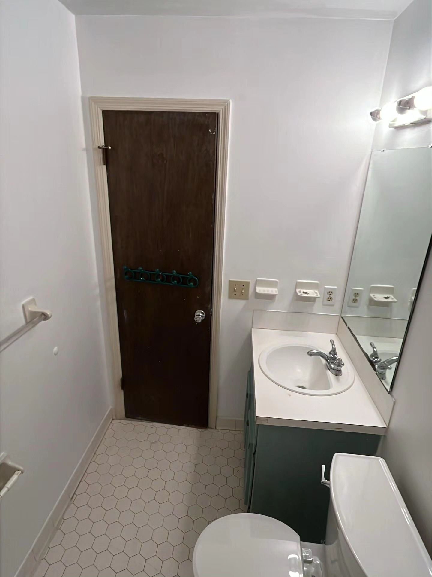 Small bathroom with sink, toilet, mirror, brown door, and white walls.
