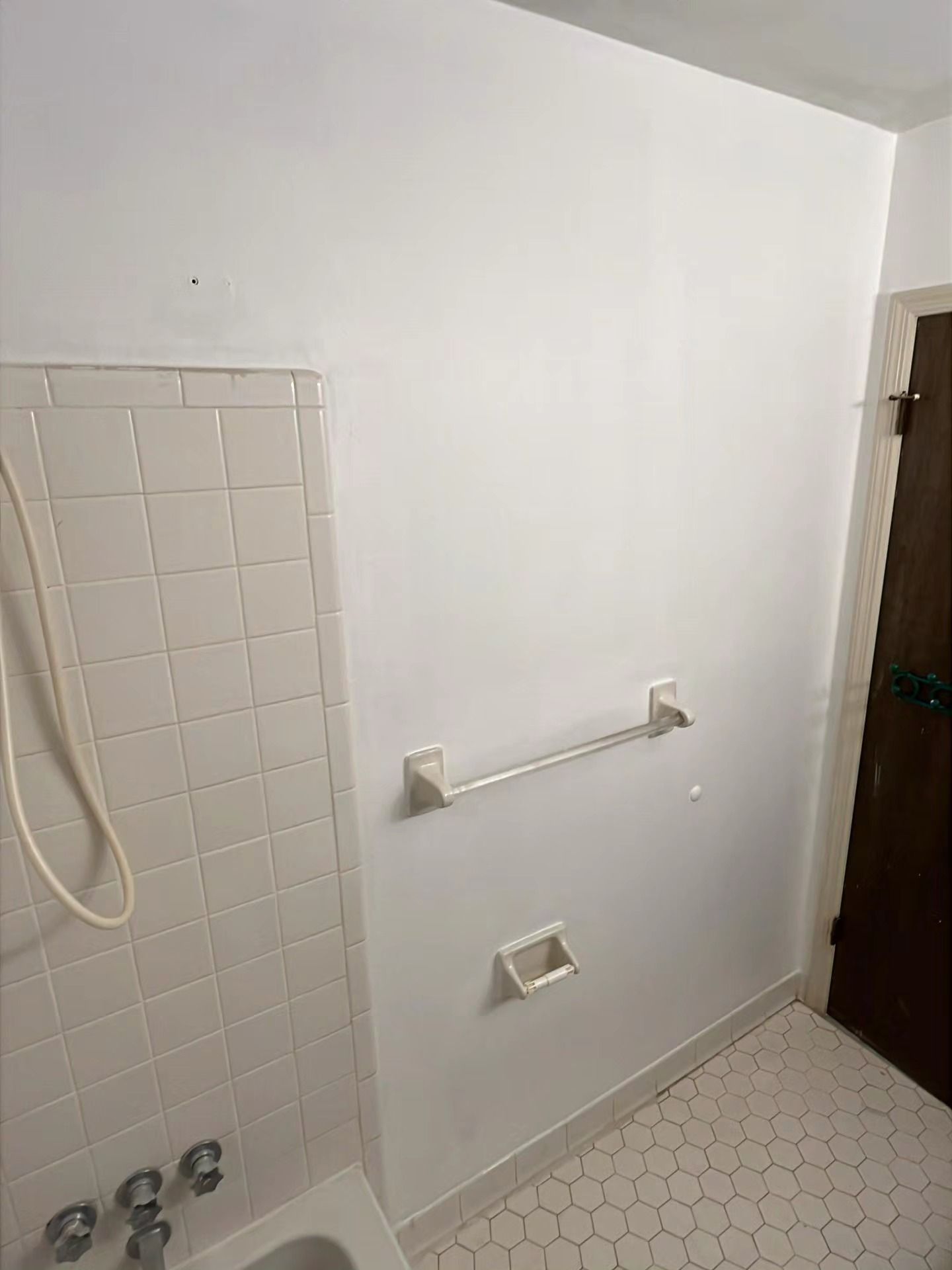 Small bathroom with tub, tiled wall, grab bars, and a wall-mounted towel bar.