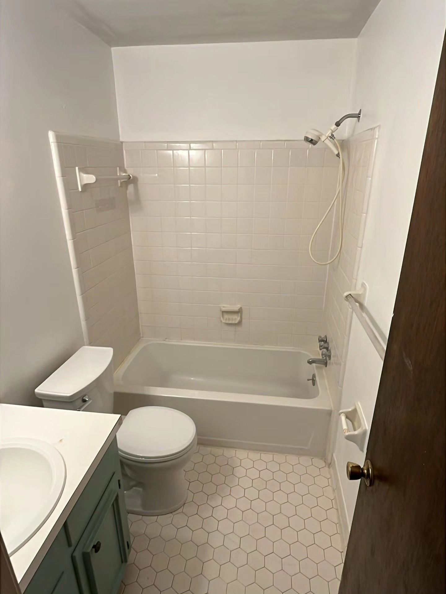 Small bathroom with tub-shower, toilet, sink, and white tile walls and floor.