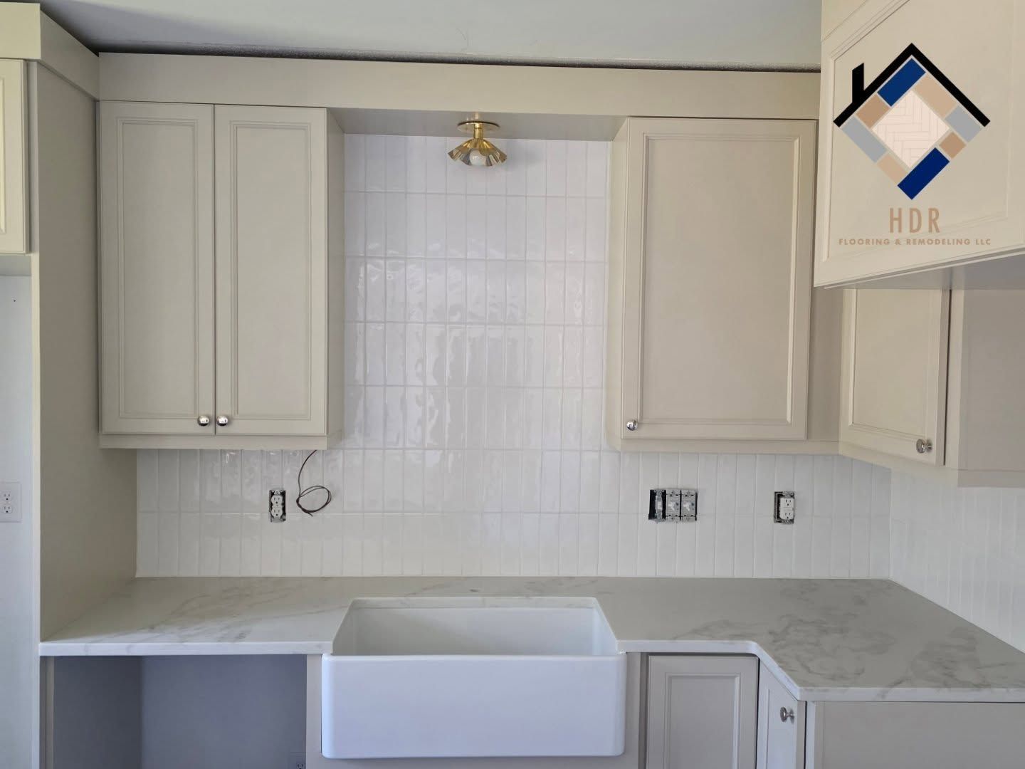 White kitchen with unfinished cabinets, gray countertop, and a farmhouse sink beneath a window.